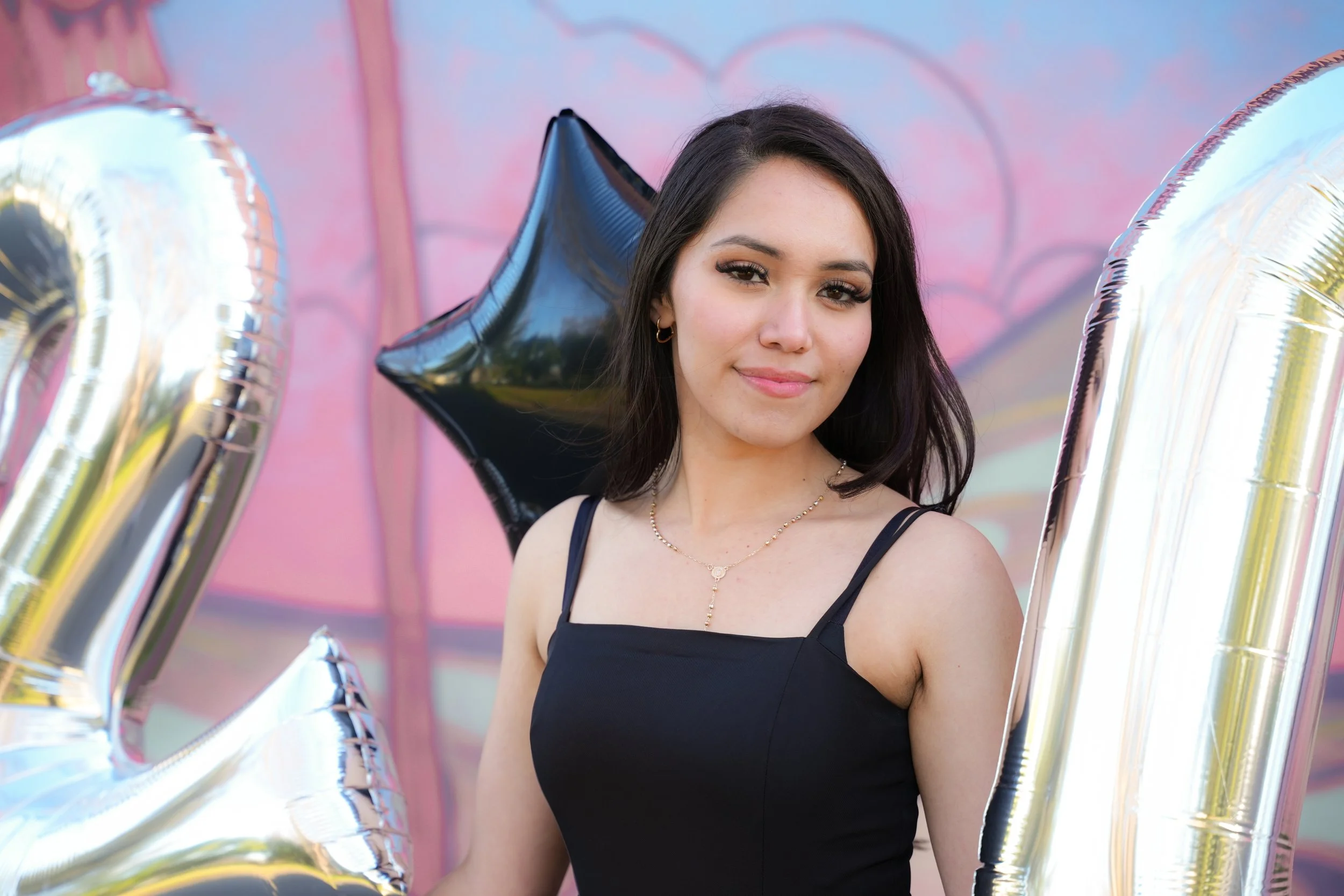 Woman in black dress holding silver and black balloons with a colorful background.