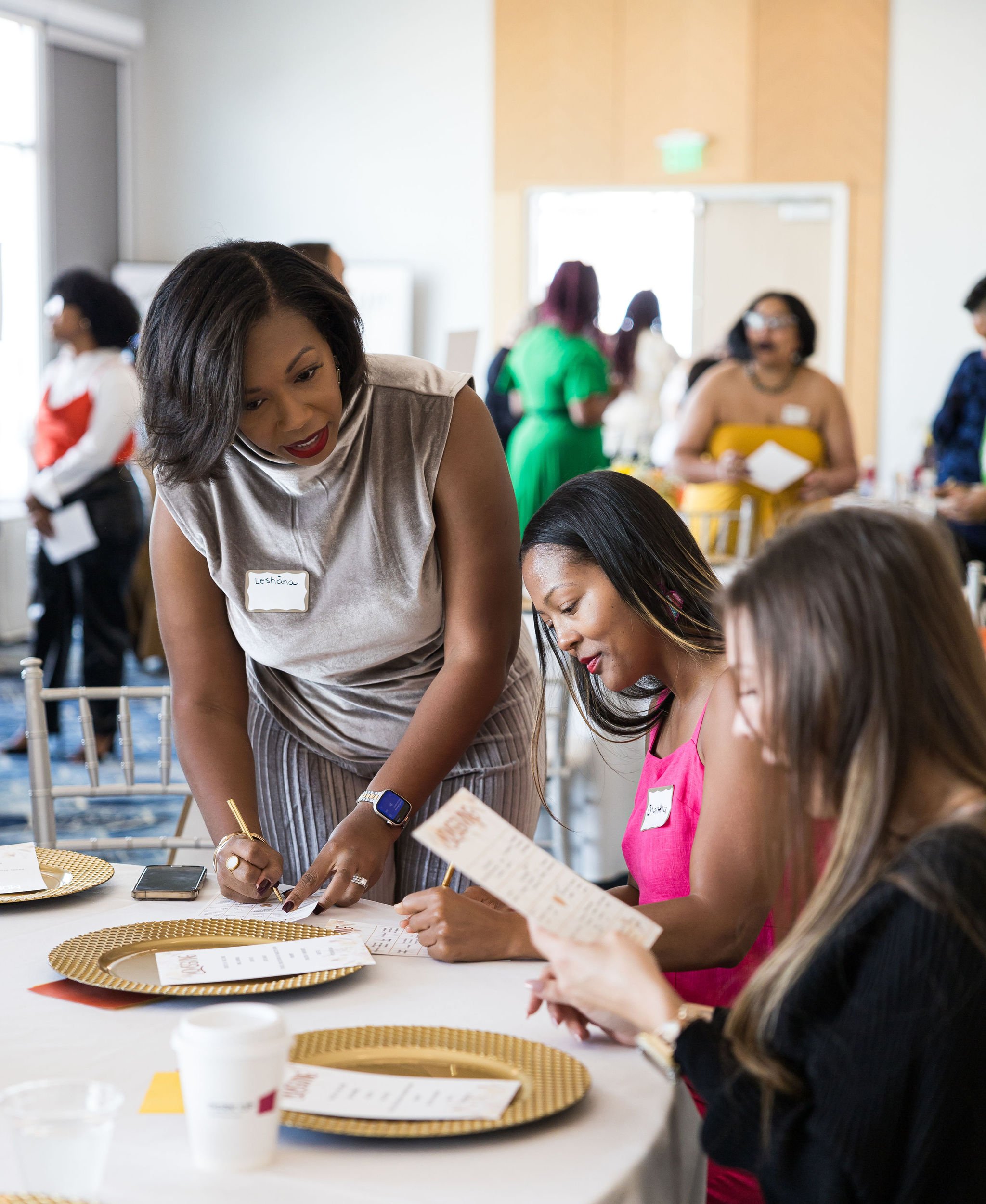 People interacting around a table at a workshop event with name tags, gold plates, and papers.
