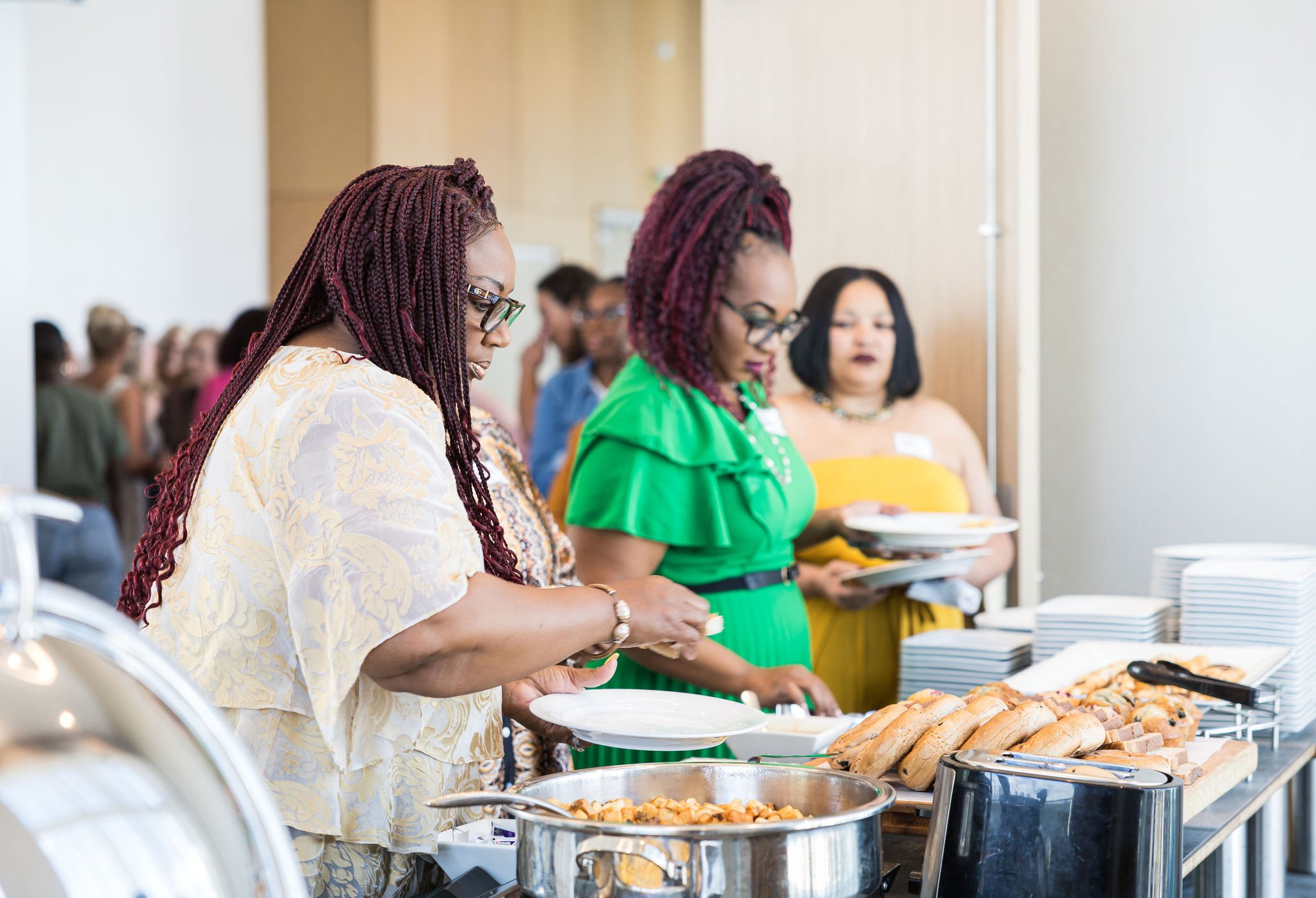 People serving themselves food at a buffet, with dishes like pastries and a pot of food on a table.