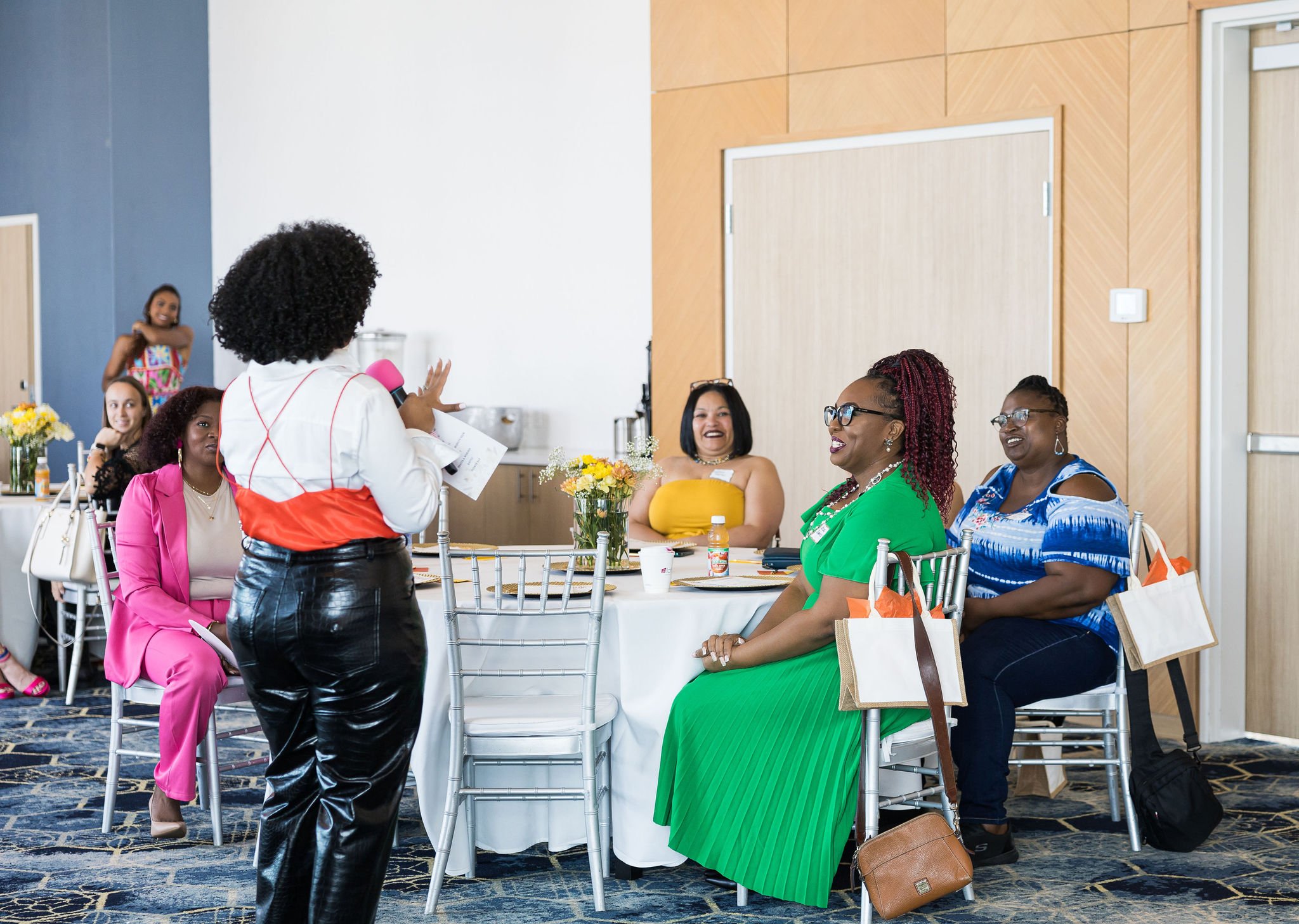 People at a networking event sitting around tables, one person speaking with a microphone.