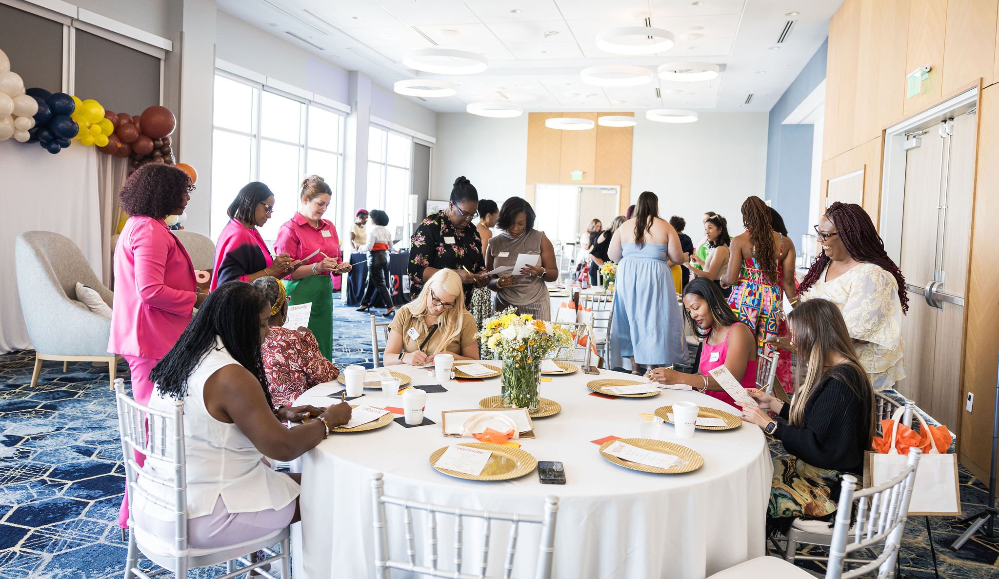 Women networking at a conference with round tables, chairs, and decorations.