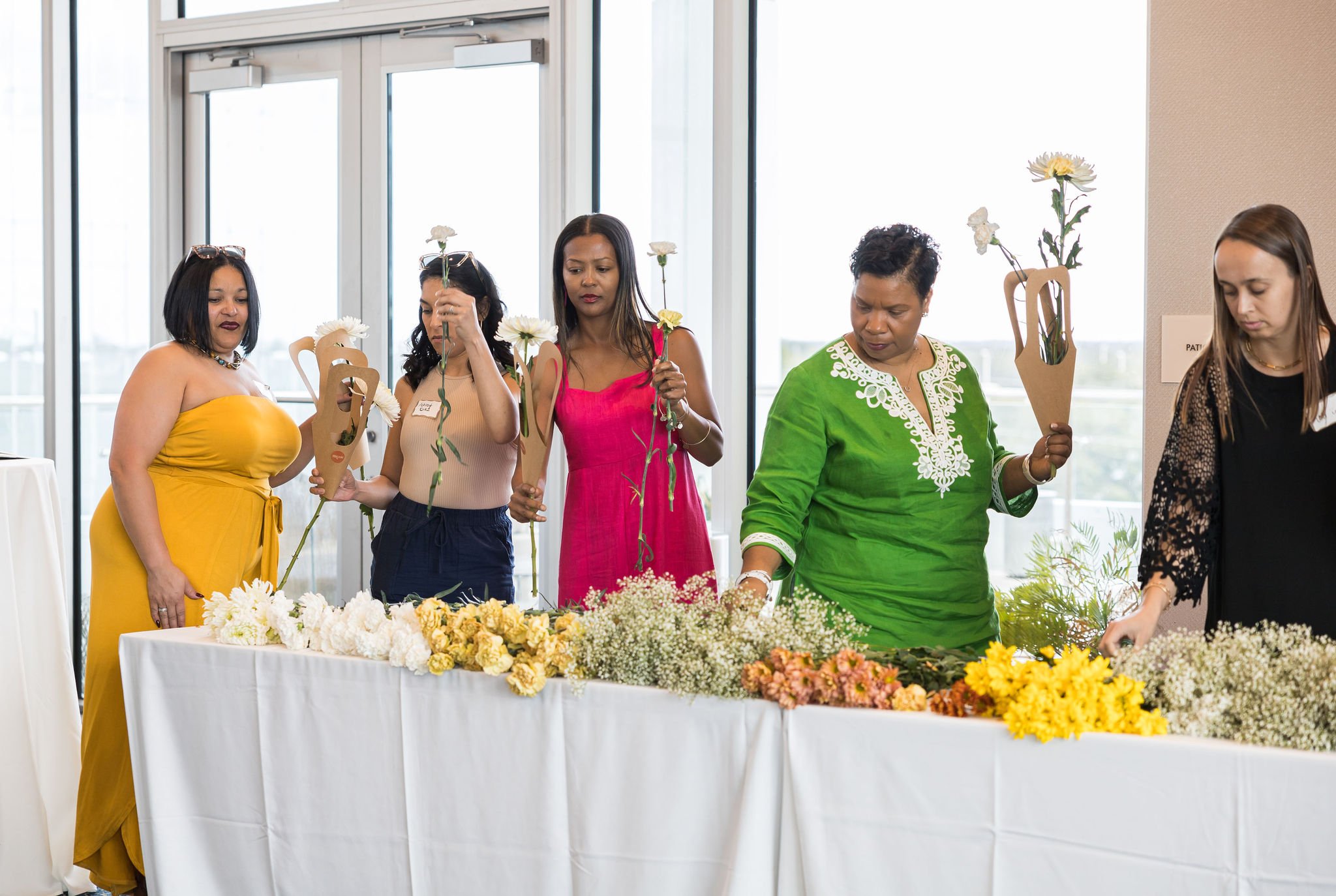 Group of women selecting flowers from a variety on a table at an indoor event.