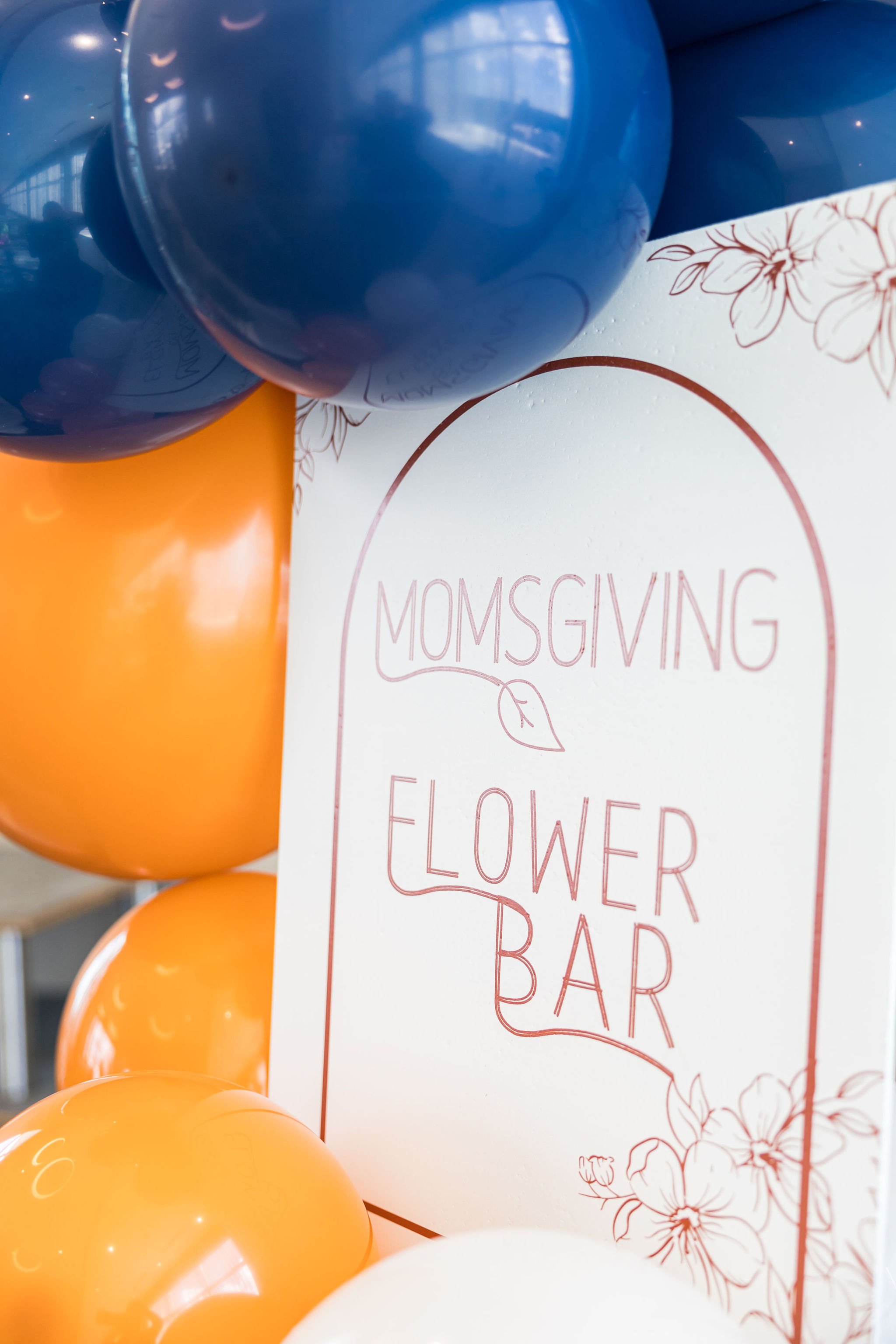Colorful balloons surrounding a "Momsgiving Flower Bar" sign.