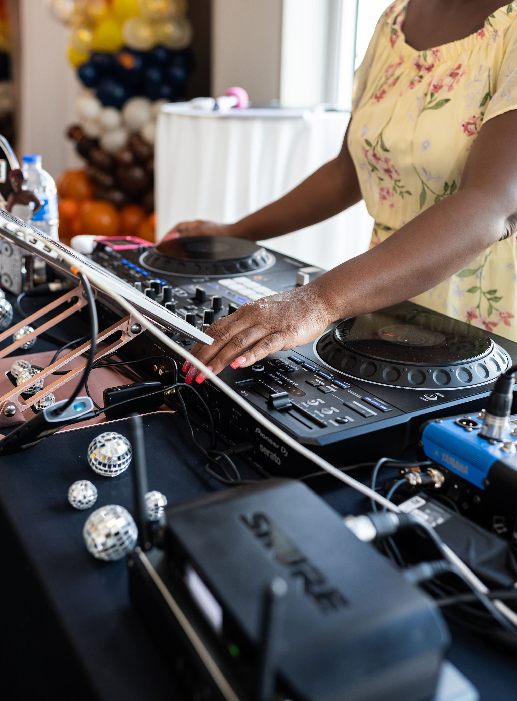 A DJ operating a mixer with colorful equipment and mini disco balls on a table.