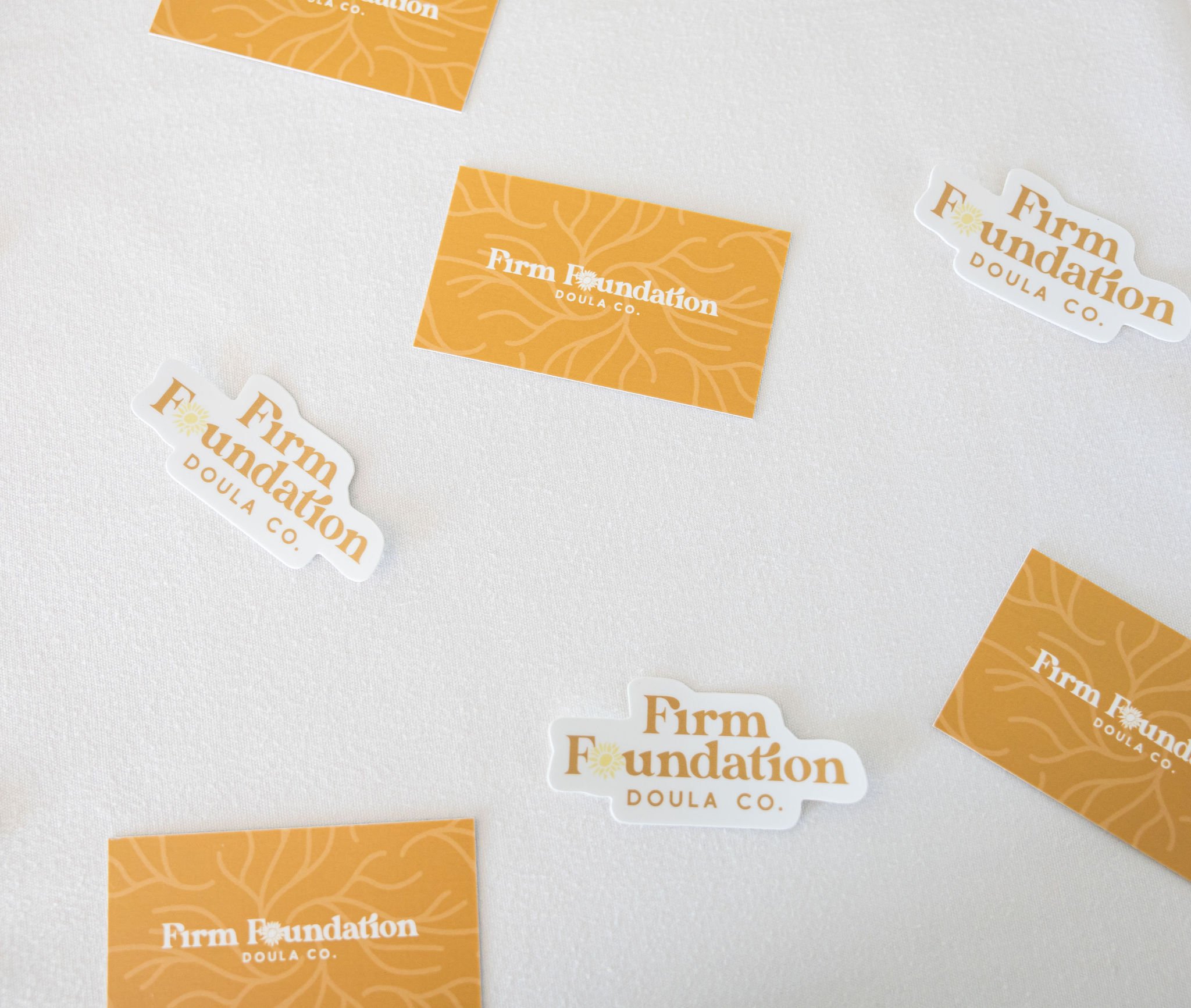 Firm Foundation Doula Co. business cards and stickers on a white surface, featuring an orange color scheme with floral patterns.
