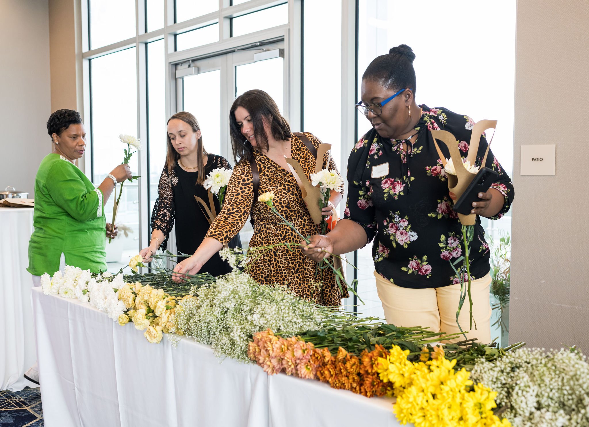 People selecting flowers from a table with various bouquets at an indoor event.