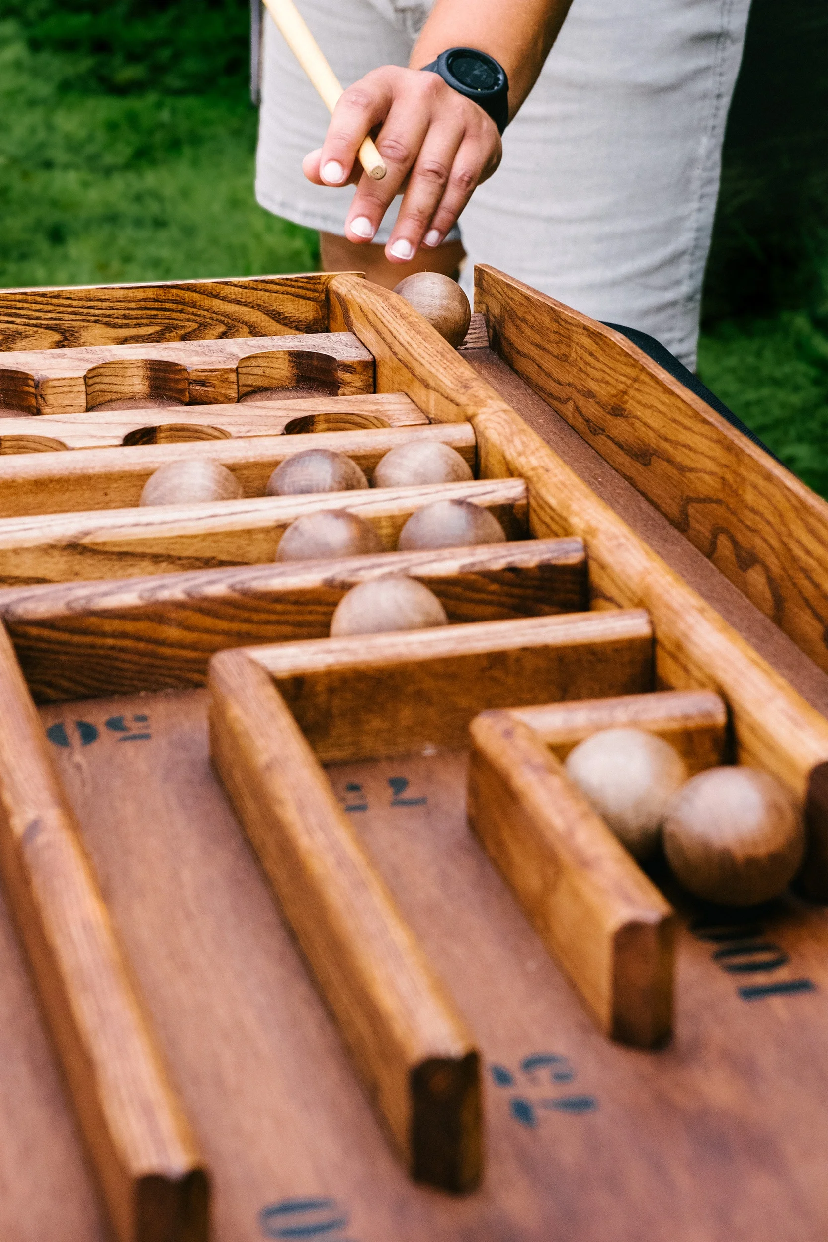 Une personne joue au billard. La personne porte une montre noire et tient une queue. Le jeu est en bois.