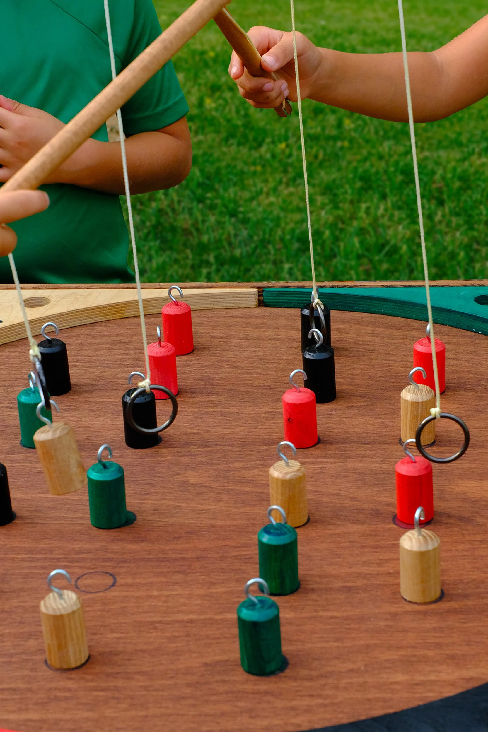 Deux enfants jouent à un jeu de société avec des cylindres colorés en bois suspendus par des fils, sur une table en bois, à l'extérieur sur de l'herbe verte.