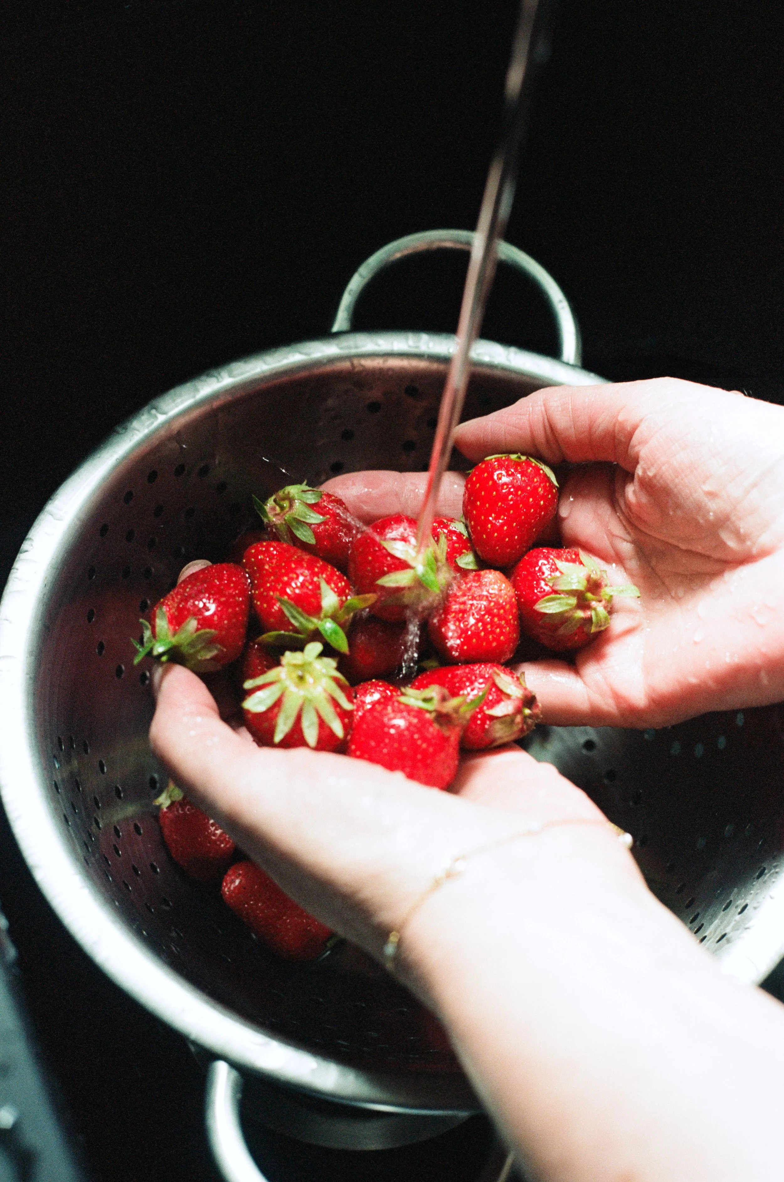 Mains lavant des fraises dans une passoire sous l'eau. Reportage