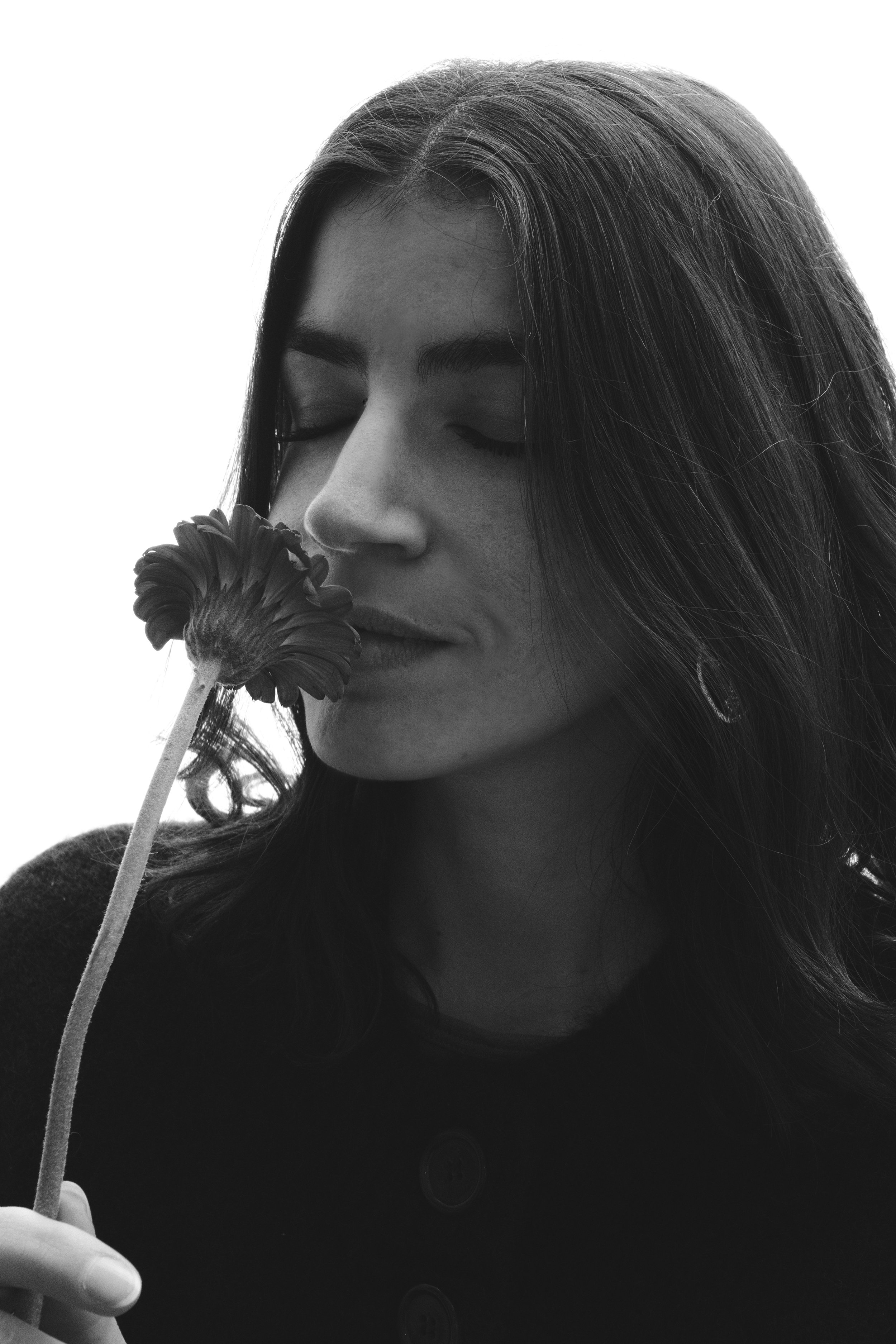 Une femme aux cheveux longs ferme les yeux en tenant une fleur près de son visage. Portrait, éditorial