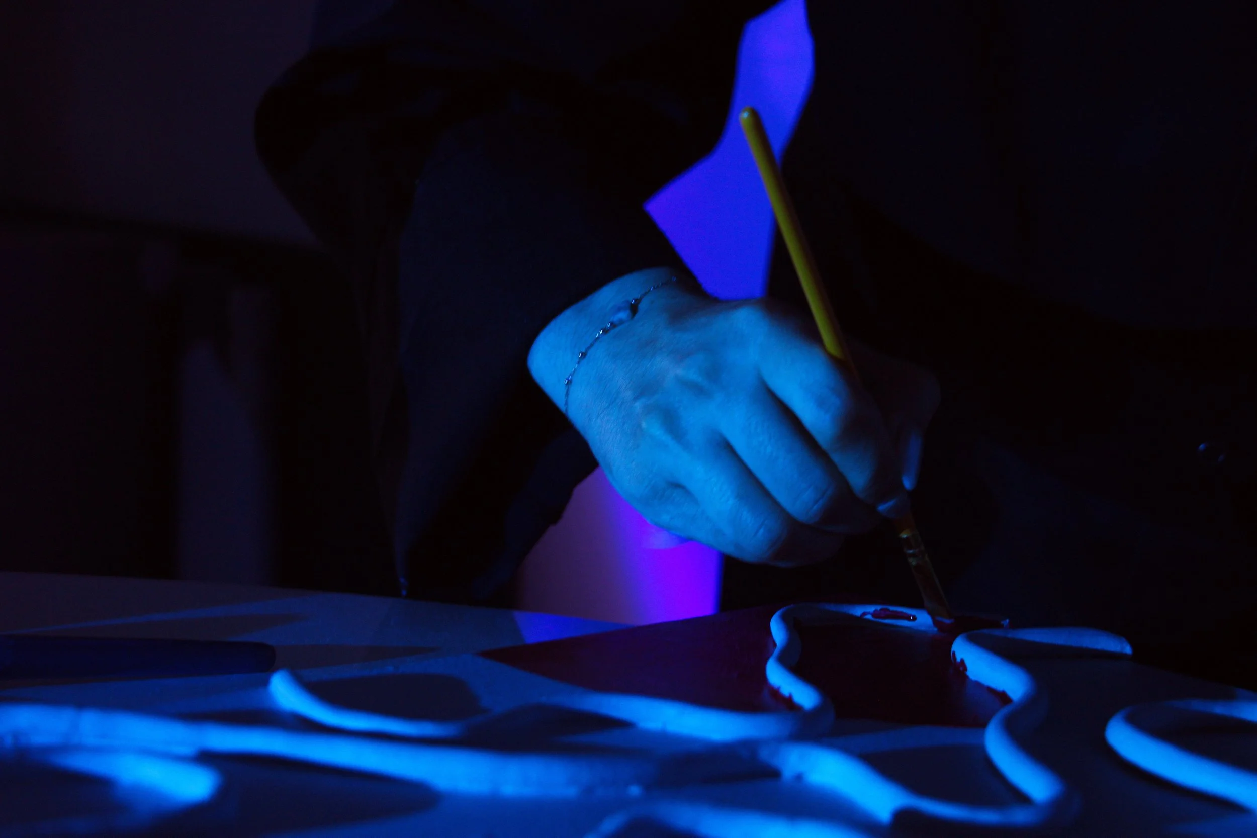 Main qui écrit avec un pinceau sur une surface illuminée par de la lumière noire dans l'obscurité. Reportage