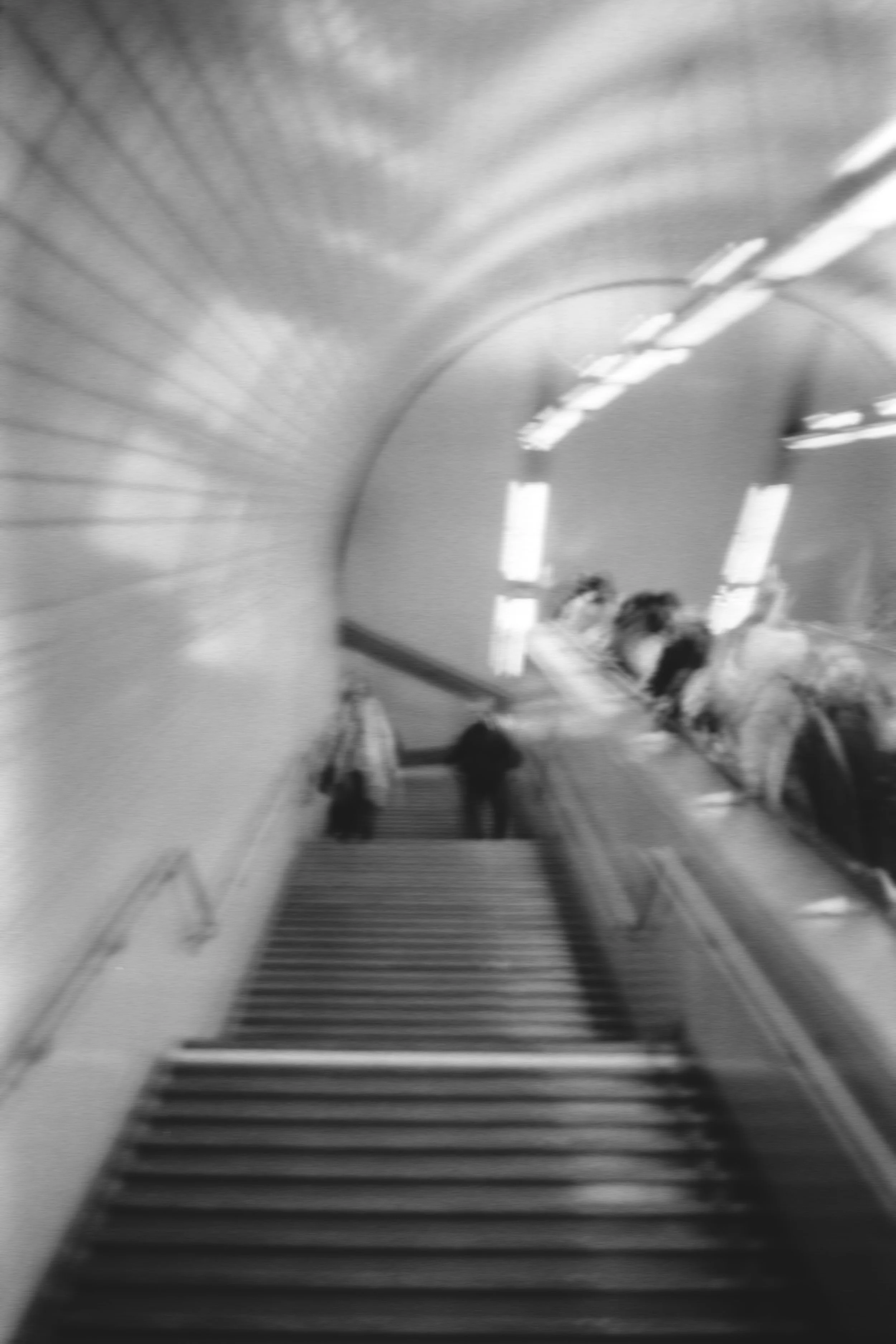 Une vue en noir et blanc d'une descente d'escalier mécanique dans une station de métro, avec des personnes qui descendent. Editorial