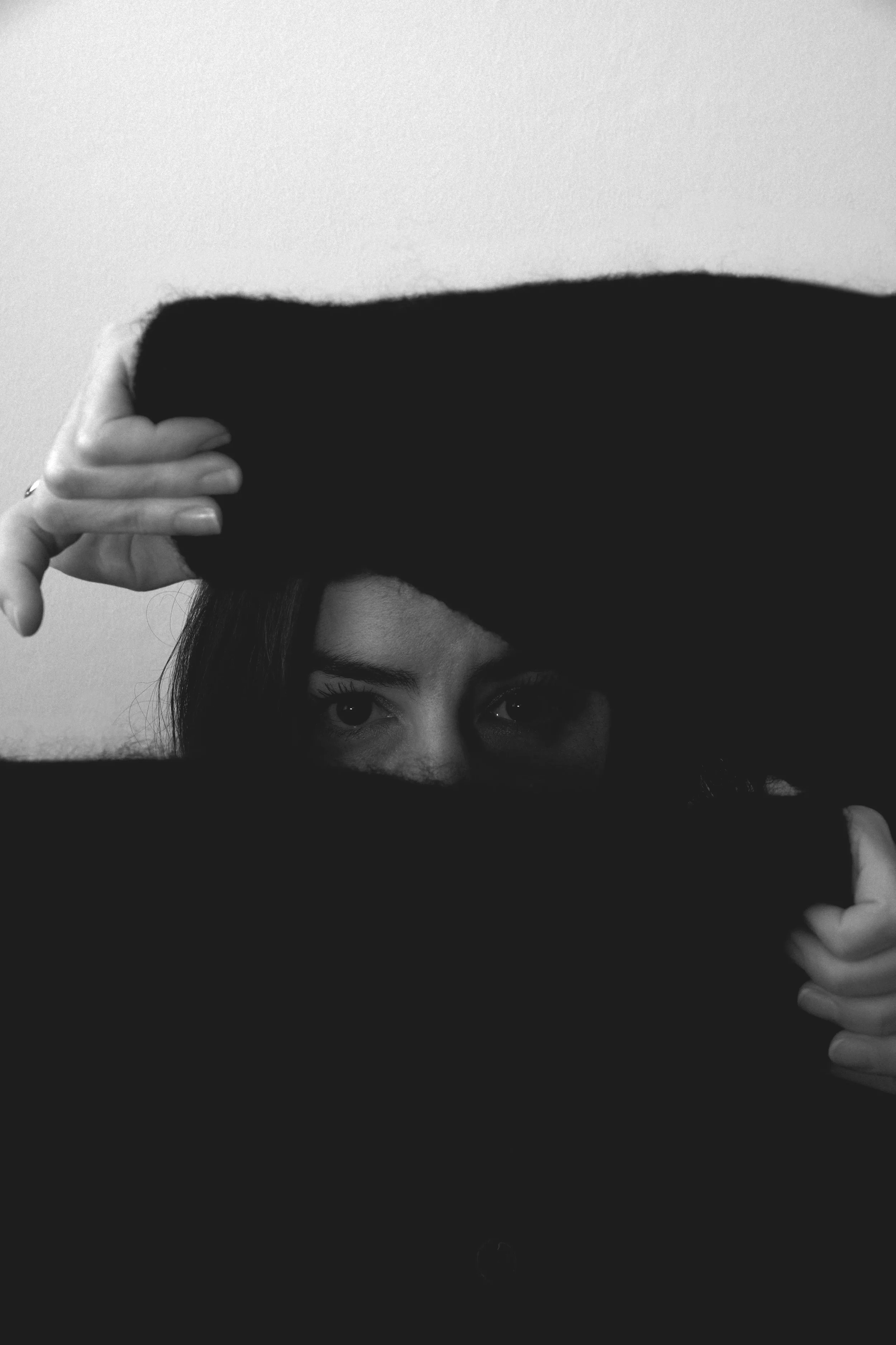 Une femme regarde par un trou dans un vêtement noir, ses yeux et partie du visage visible. Portrait / éditorial