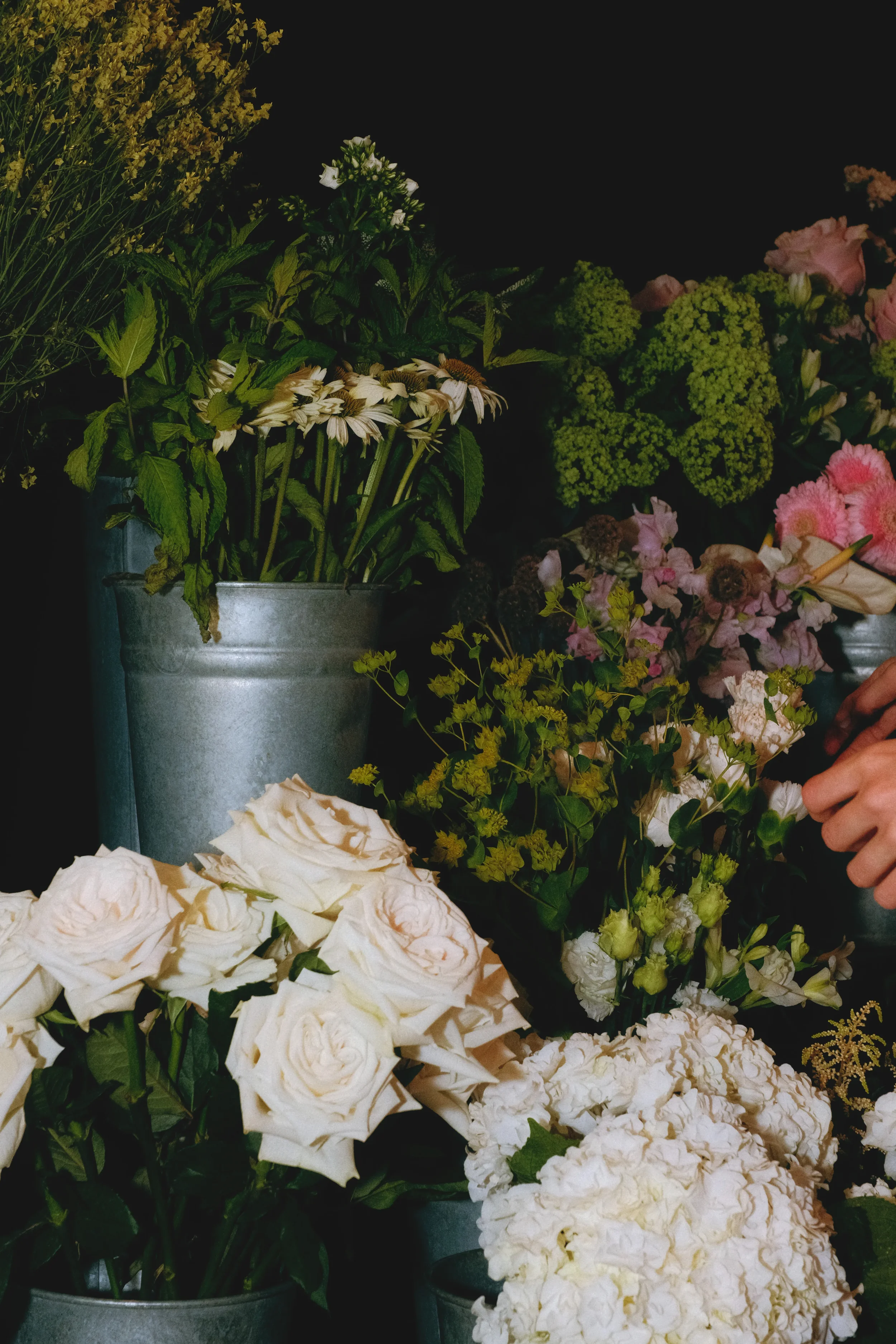 Fleurs de différentes couleurs et types dans des vases en métal, organisées en bouquet, sur fond noir.