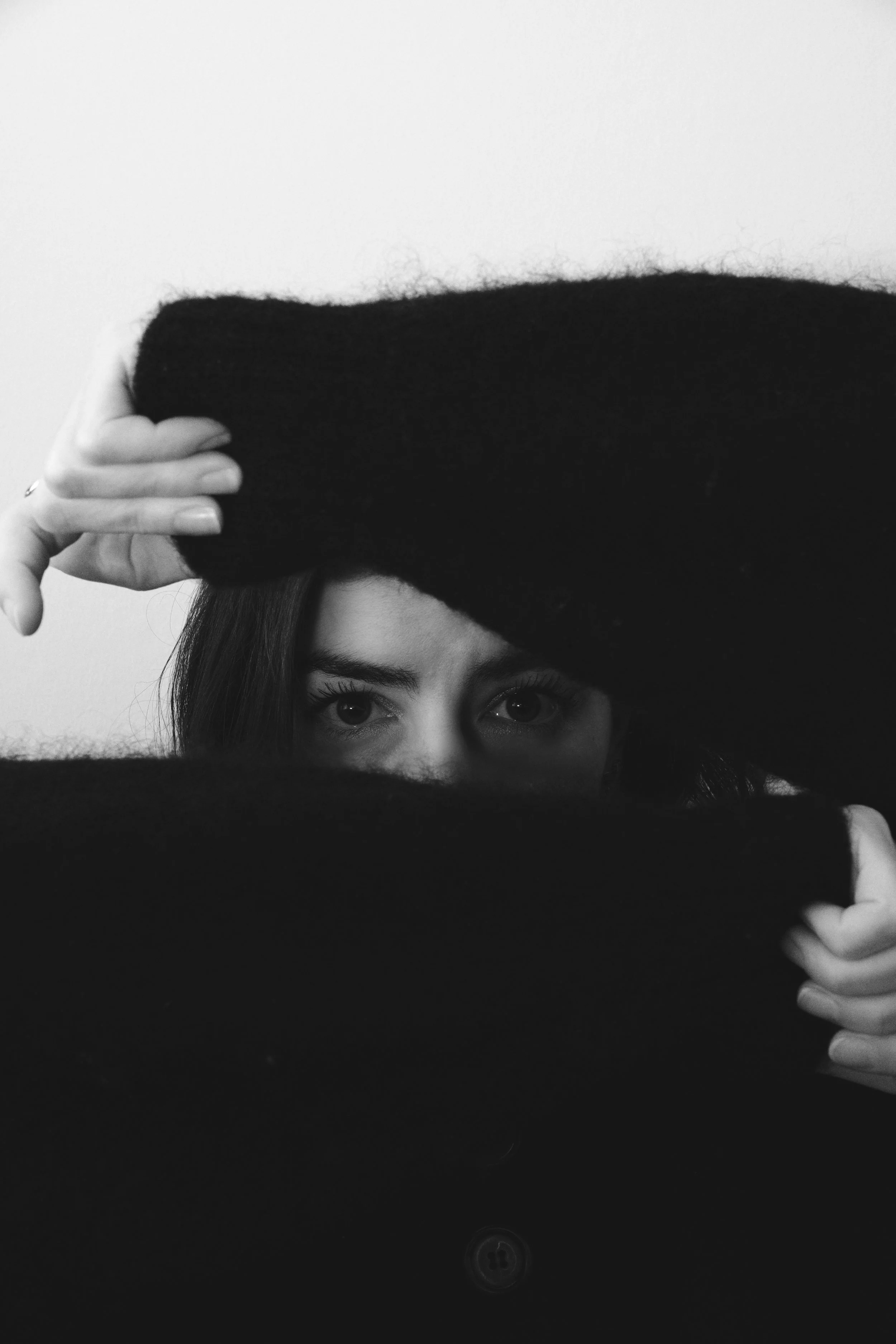 Une femme regarde par un trou dans un vêtement noir, ses yeux et partie du visage visible. Portrait / éditorial