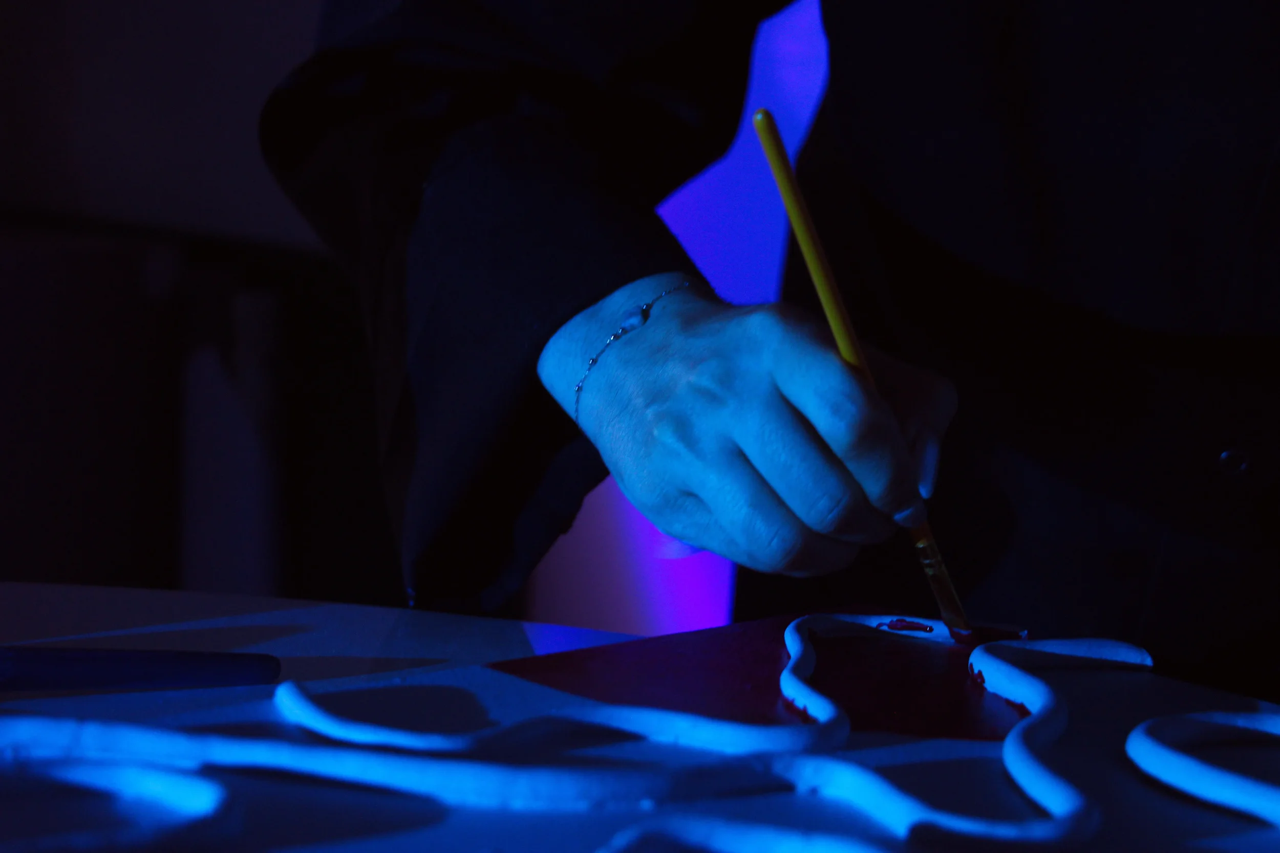 Main en train de peindre dans une pièce sombre, illuminée par une lumière bleue.