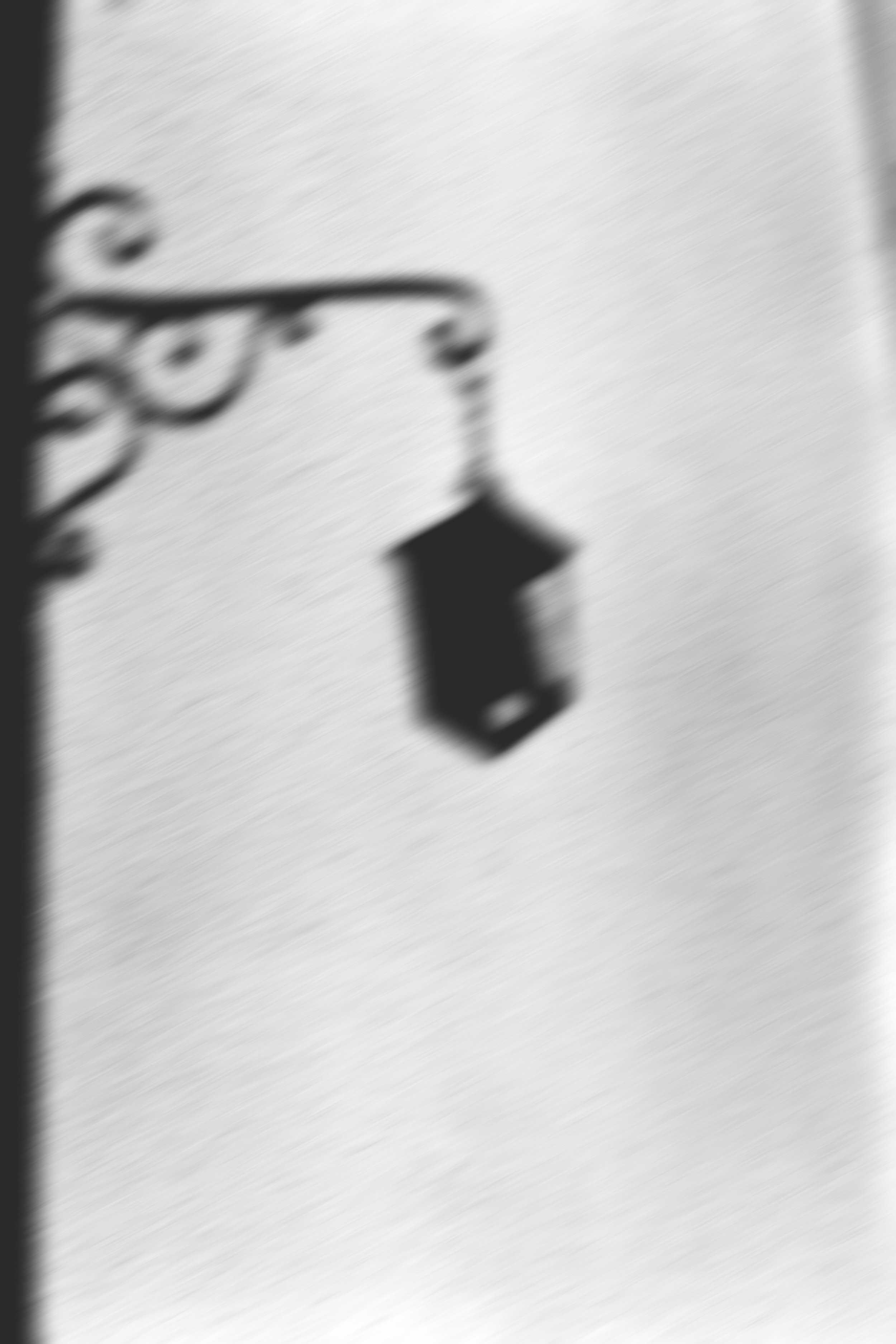 Une lampe suspendue avec un abat-jour noir, vue à travers une fenêtre avec une grille en fer forgé, en noir et blanc, floue. Editorial