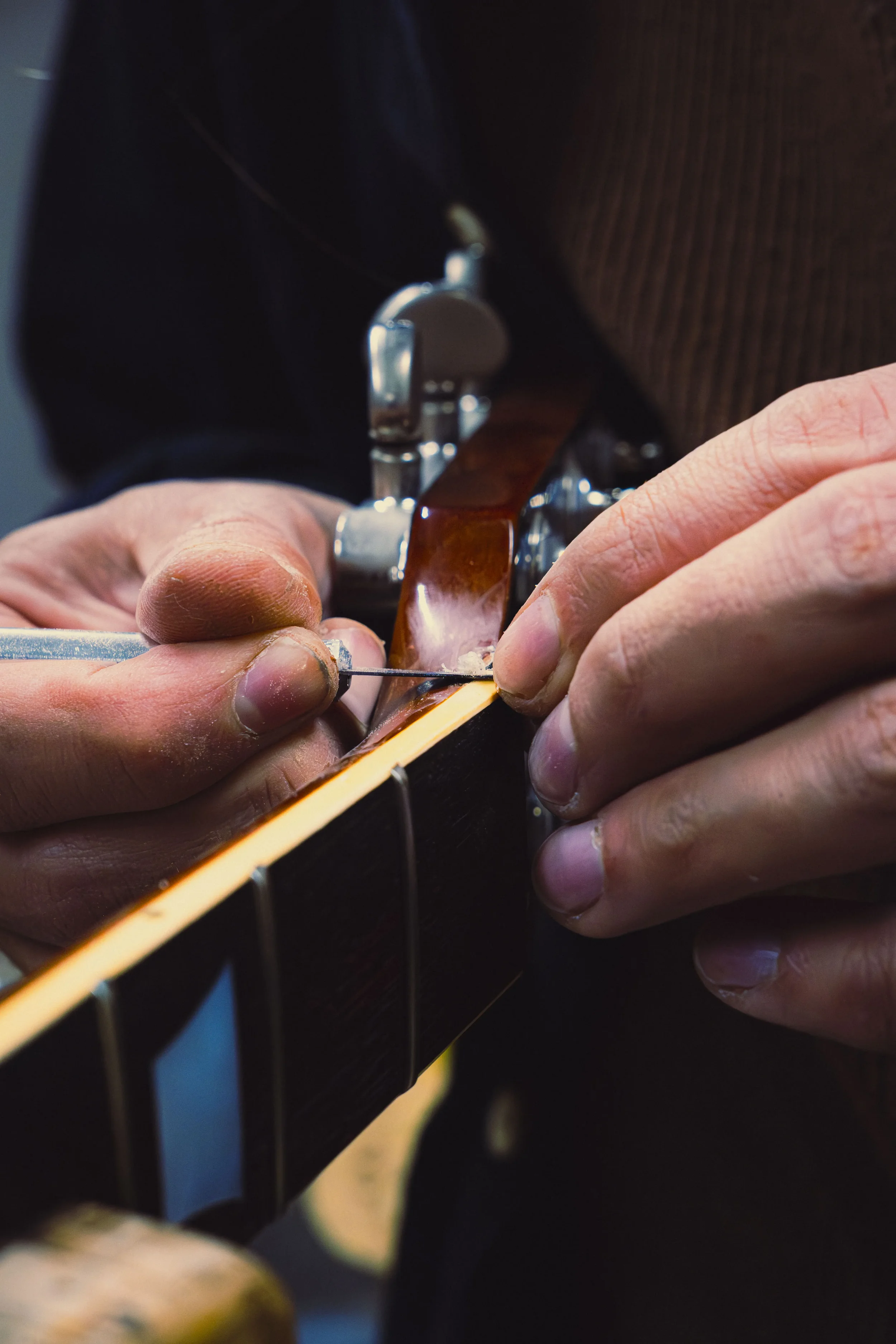 Photo en couleurs, on y voit des mains réparant un manche de guitare. Reportage