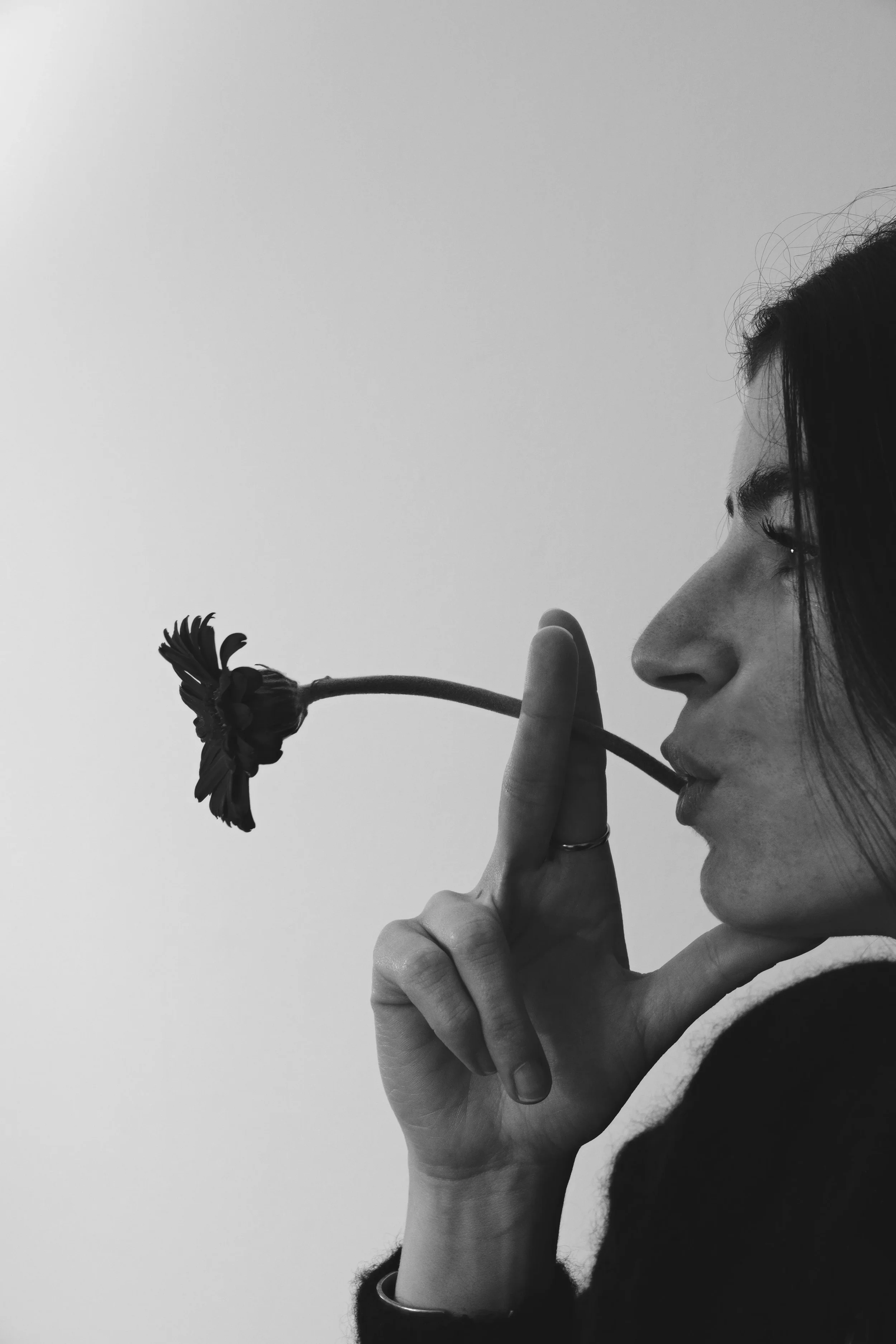 Une femme en profil tient une fleur recourbée vers ses lèvres, en noir et blanc. Editorial / portrait