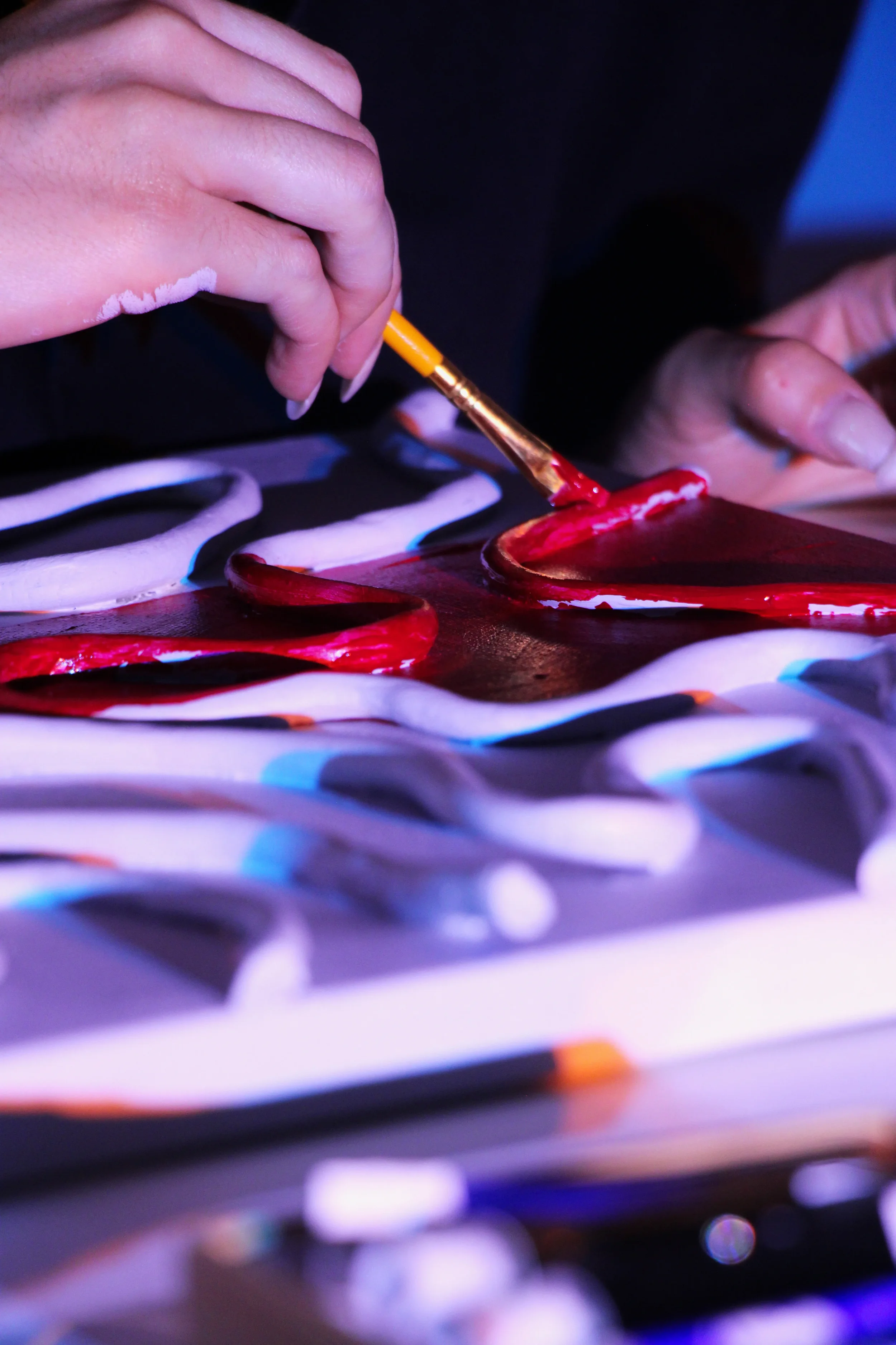 Main peignant avec un pinceau une surface colorée, zones de peinture en rouge, blanc et noir, sous une lumière tamisée.