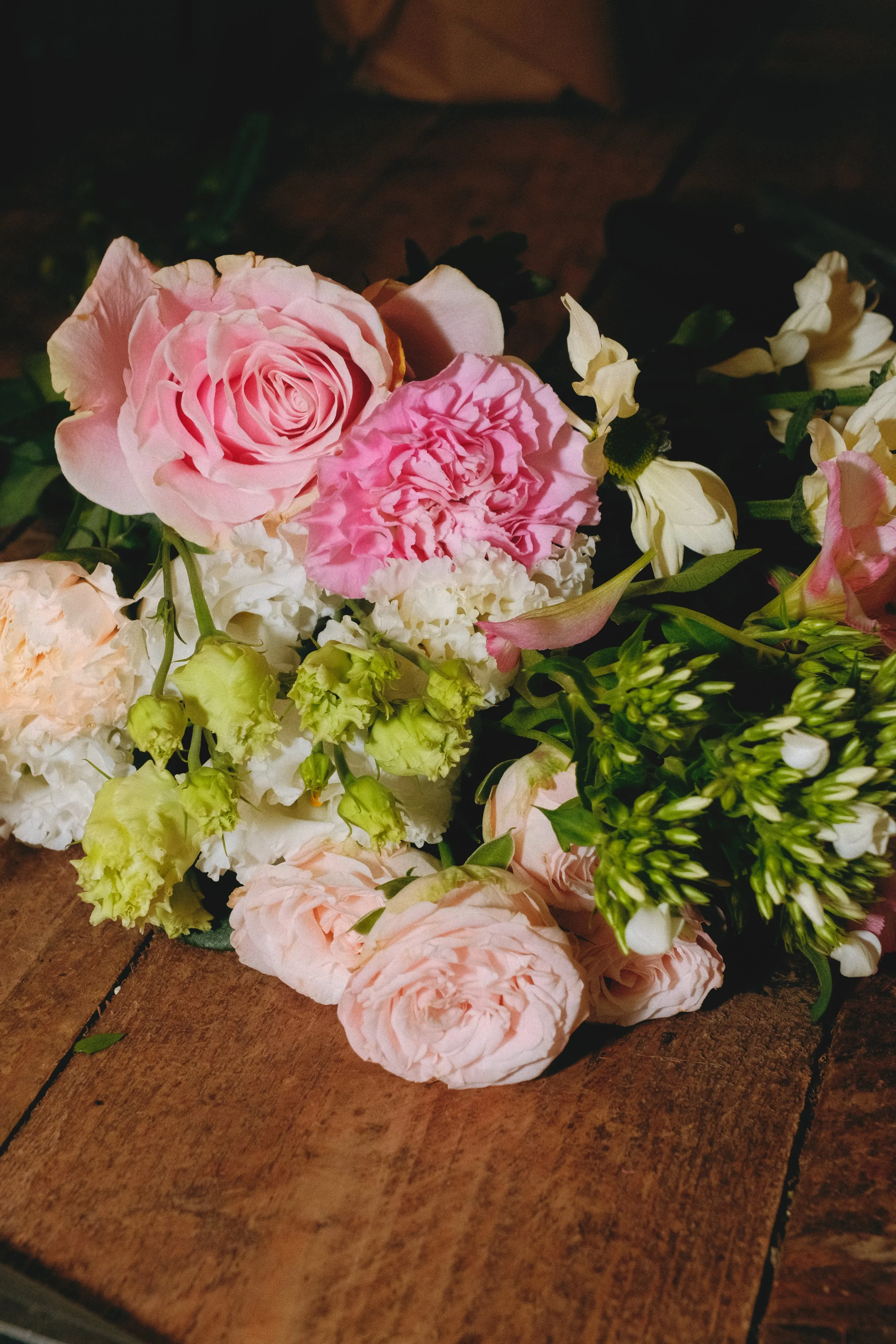 Un bouquet de fleurs avec des roses roses, des hortensias rose et blancs, et des fleurs blanches, posé sur un plancher en bois. Reportage