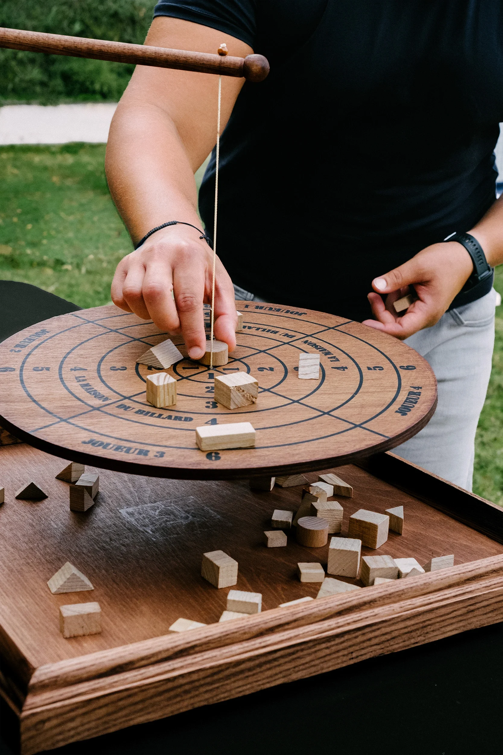 Une personne joue au jeu en bois utilisant ses doigts pour déplacer des pièces en bois sur un plateau circulaire avec des cercles et des inscriptions.
