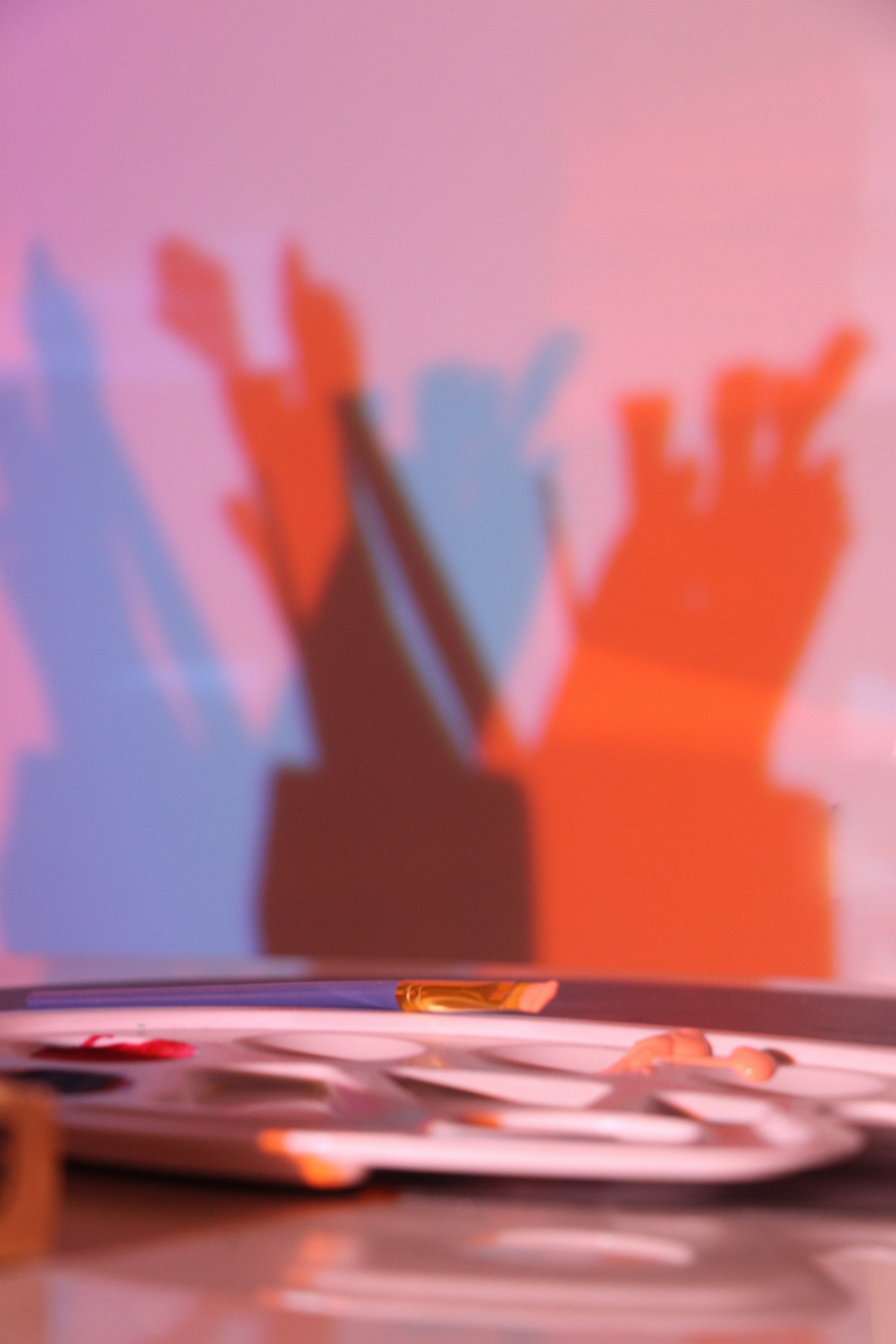 Ombres de mains projetées sur un mur rose avec une palette de peinture et des pinceaux au premier plan. Reportage