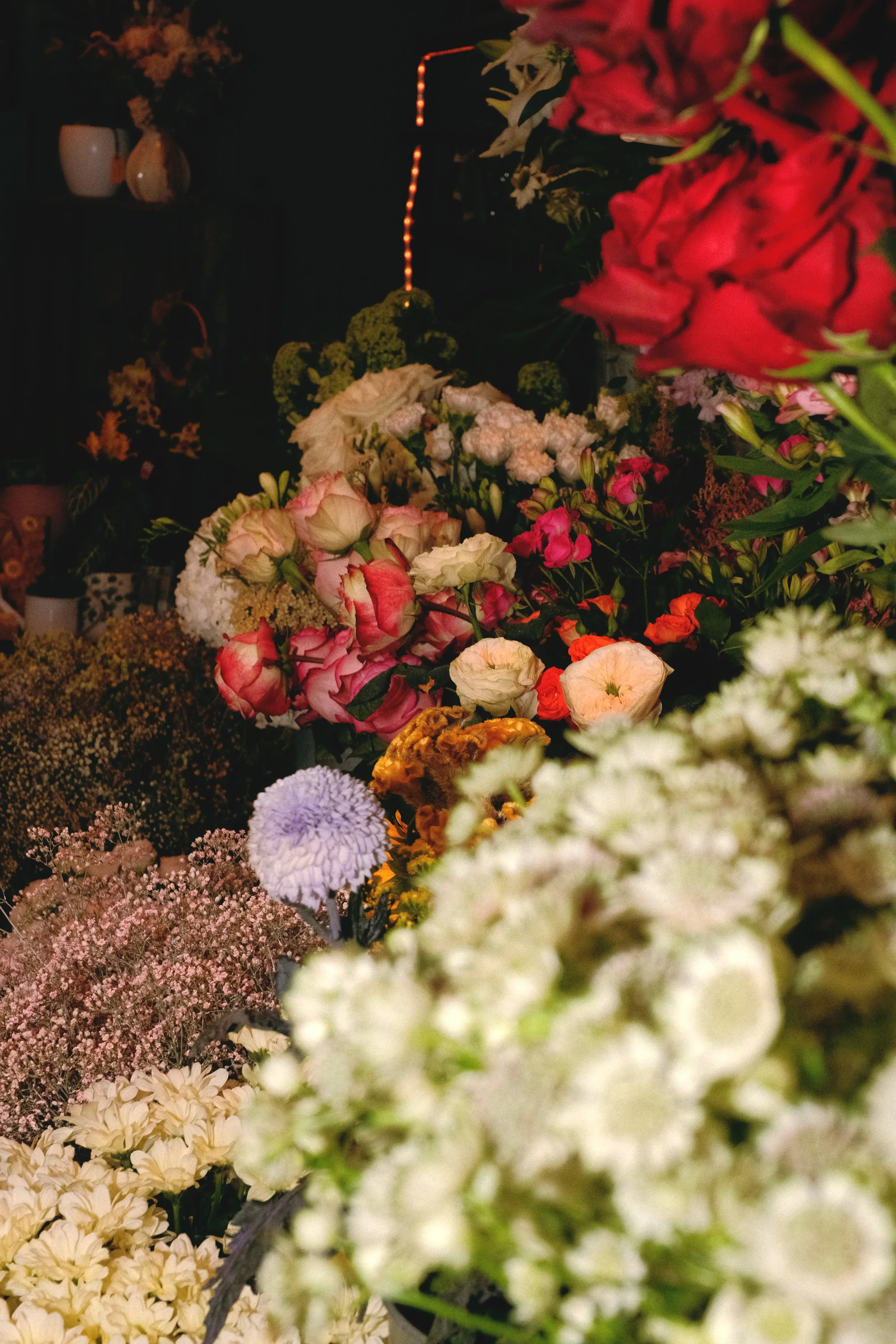 Une scène nocturne avec une multitude de fleurs colorées et variées, notamment des roses, des marguerites, et des fleurs de diverses espèces, disposées en bouquets délirants, avec un fond sombre et quelques sources de lumière douce.
