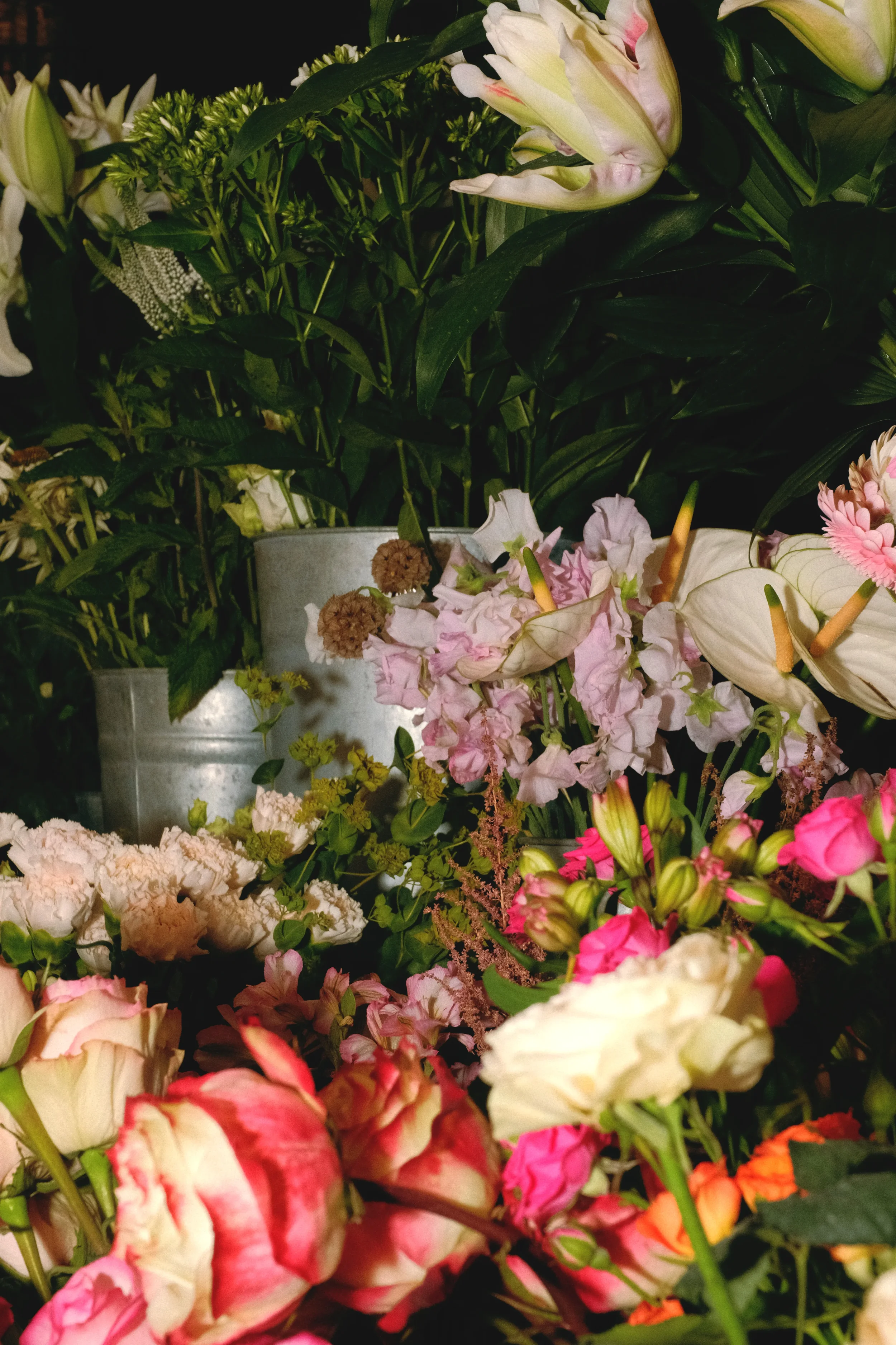 Arrangement floral avec différentes fleurs colorées, incluant des lys, des roses, et d'autres fleurs variées dans des vases en métal.