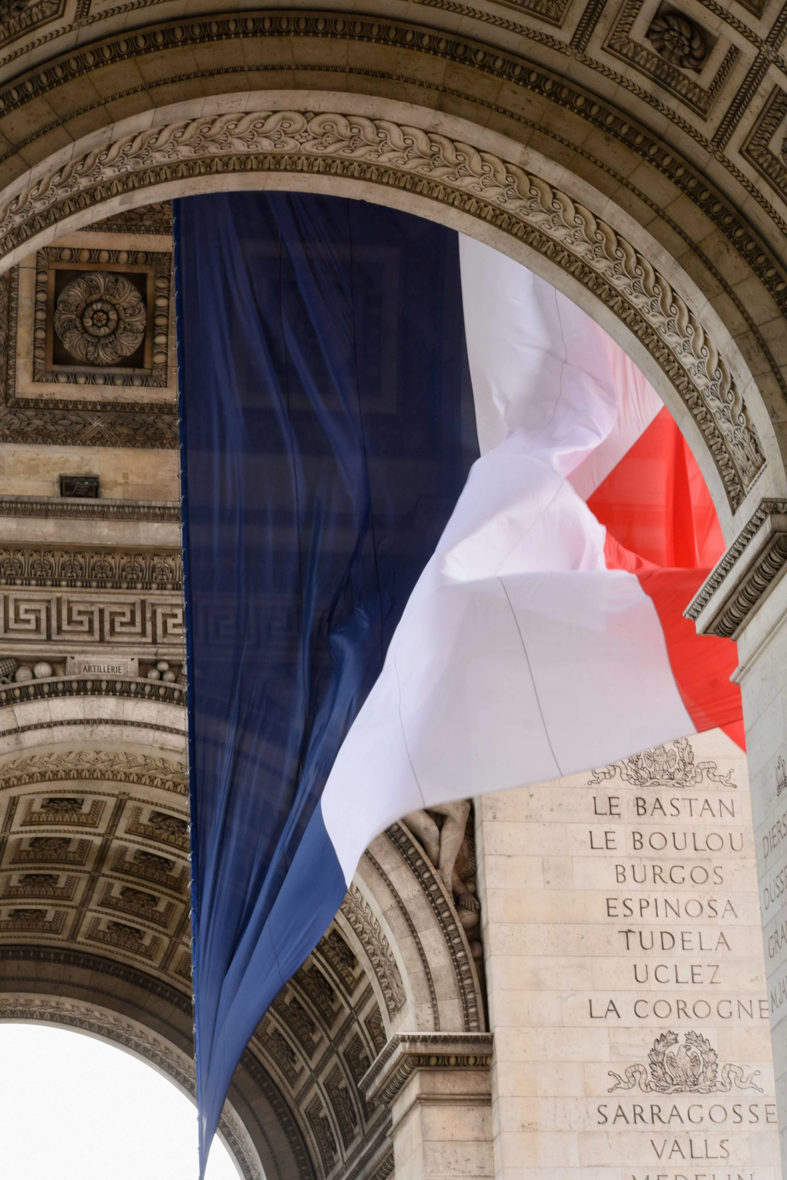 Drapeau tricolore français suspendu sous l'Arc de Triomphe à Paris.