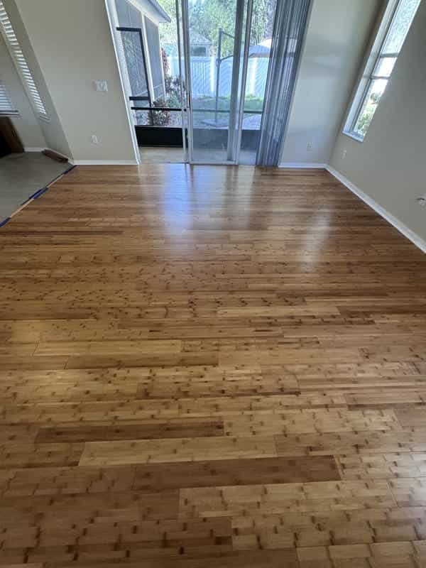 Empty room with light wood flooring, sliding glass door leading to outdoor patio, and windows allowing natural light inside. Own Style Flooring