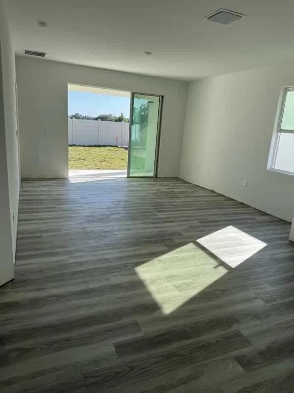 Empty room with new wood laminate flooring, white walls, and a sliding glass door leading to a backyard with a white fence. Own Style Flooring