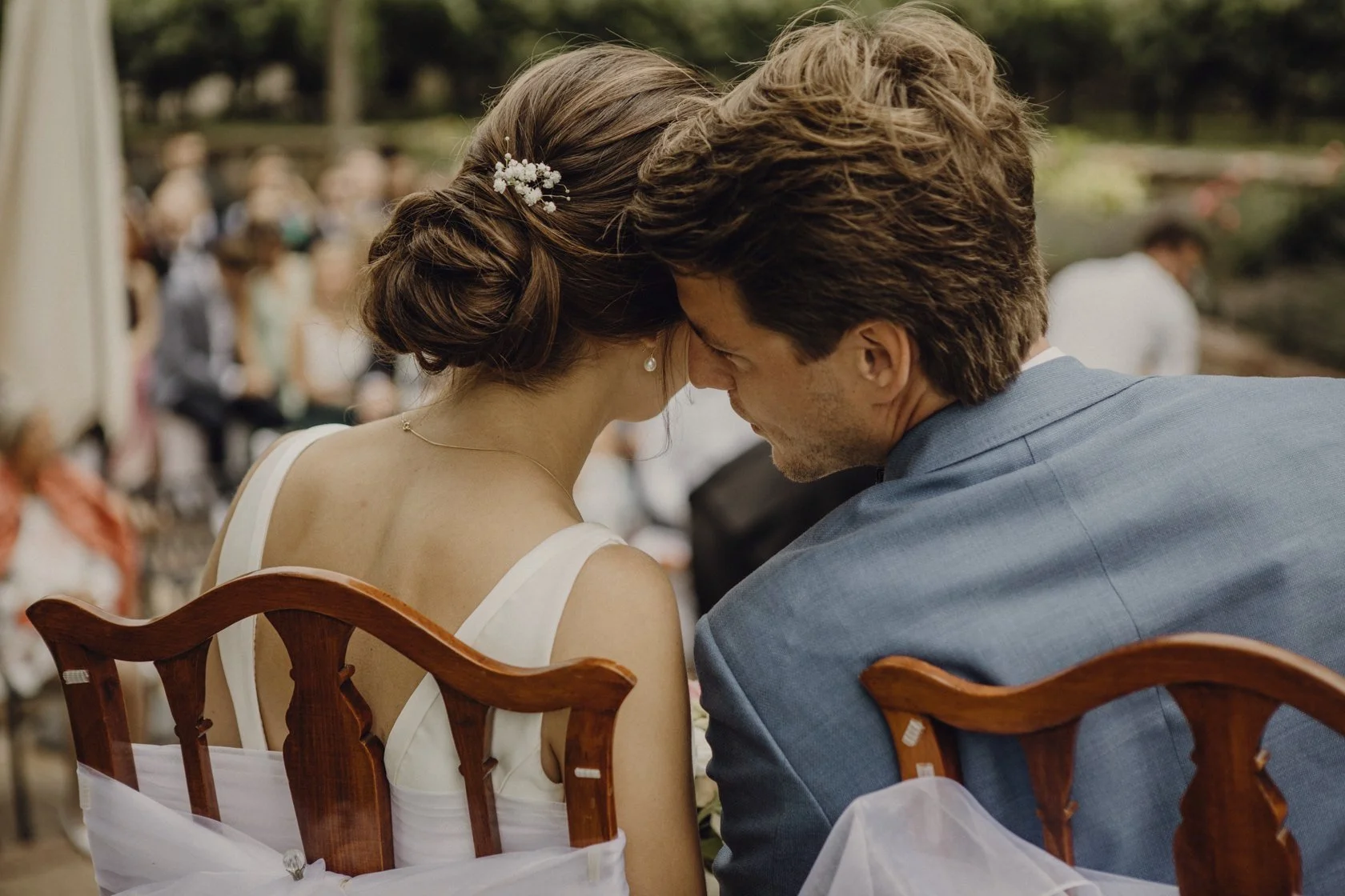 Rückansicht eines Brautpaars, das sich bei einer Hochzeit auf Stühlen zueinander lehnt.