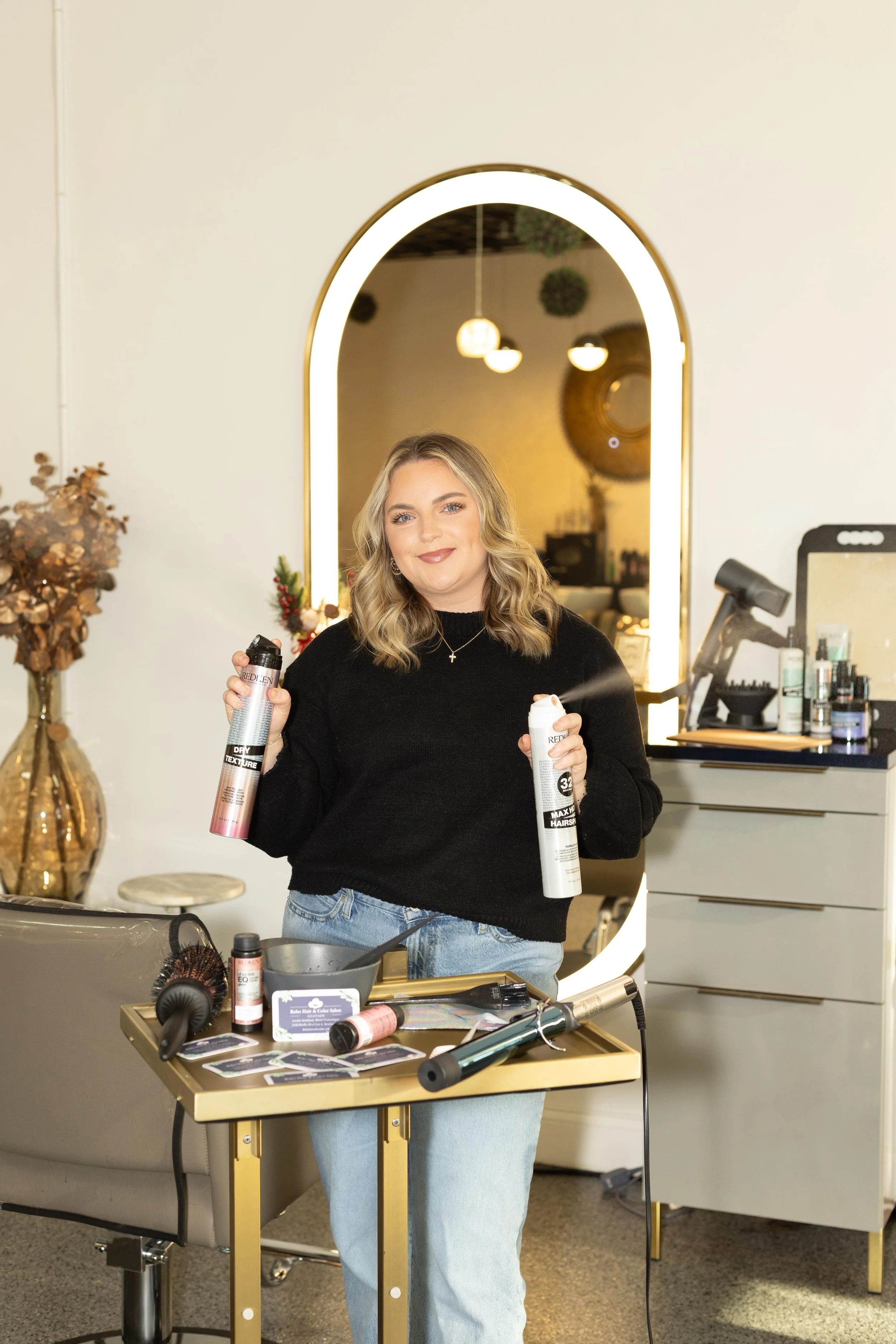 A young woman with blond hair and blue eyes standing outdoors during sunset, wearing a white sleeveless dress and holding a black jacket over her shoulder, with trees and a curving road in the background.