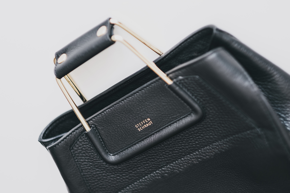 Schwarze Ledertasche mit goldfarbenen Griffen und Markenaufdruck.