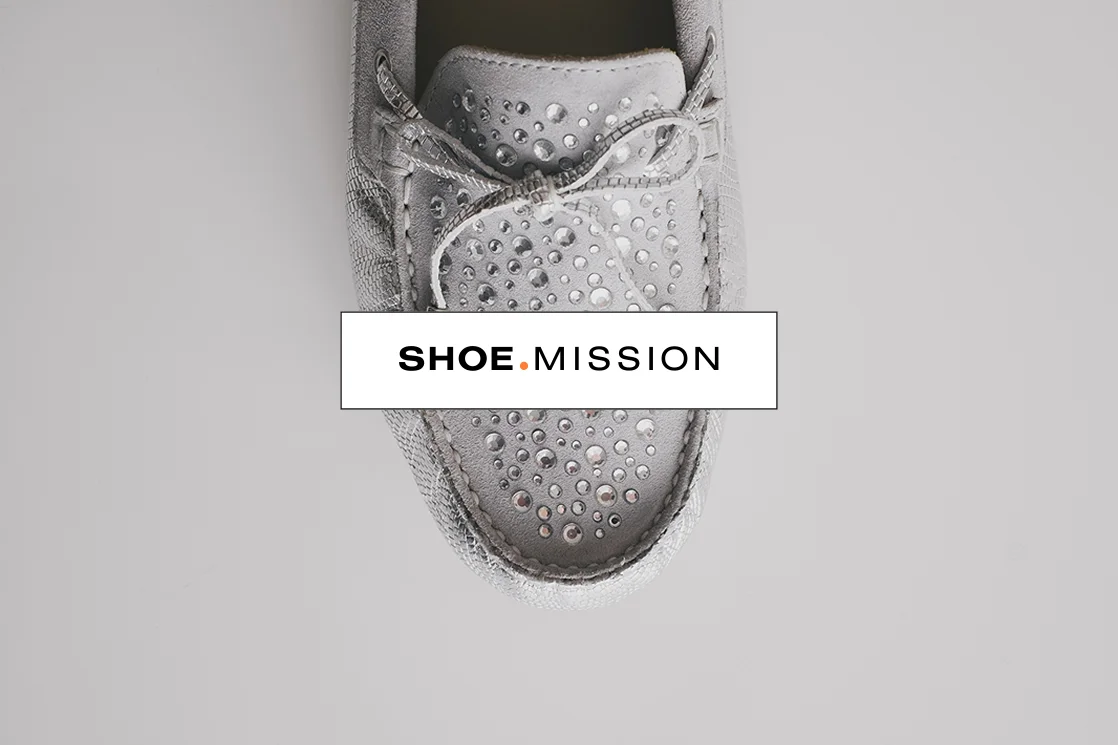 Grauer Mokassin mit Glitzersteinen und Schnürsenkeln, darüber Text "SHOE.MISSION" auf einem weißen Hintergrund.