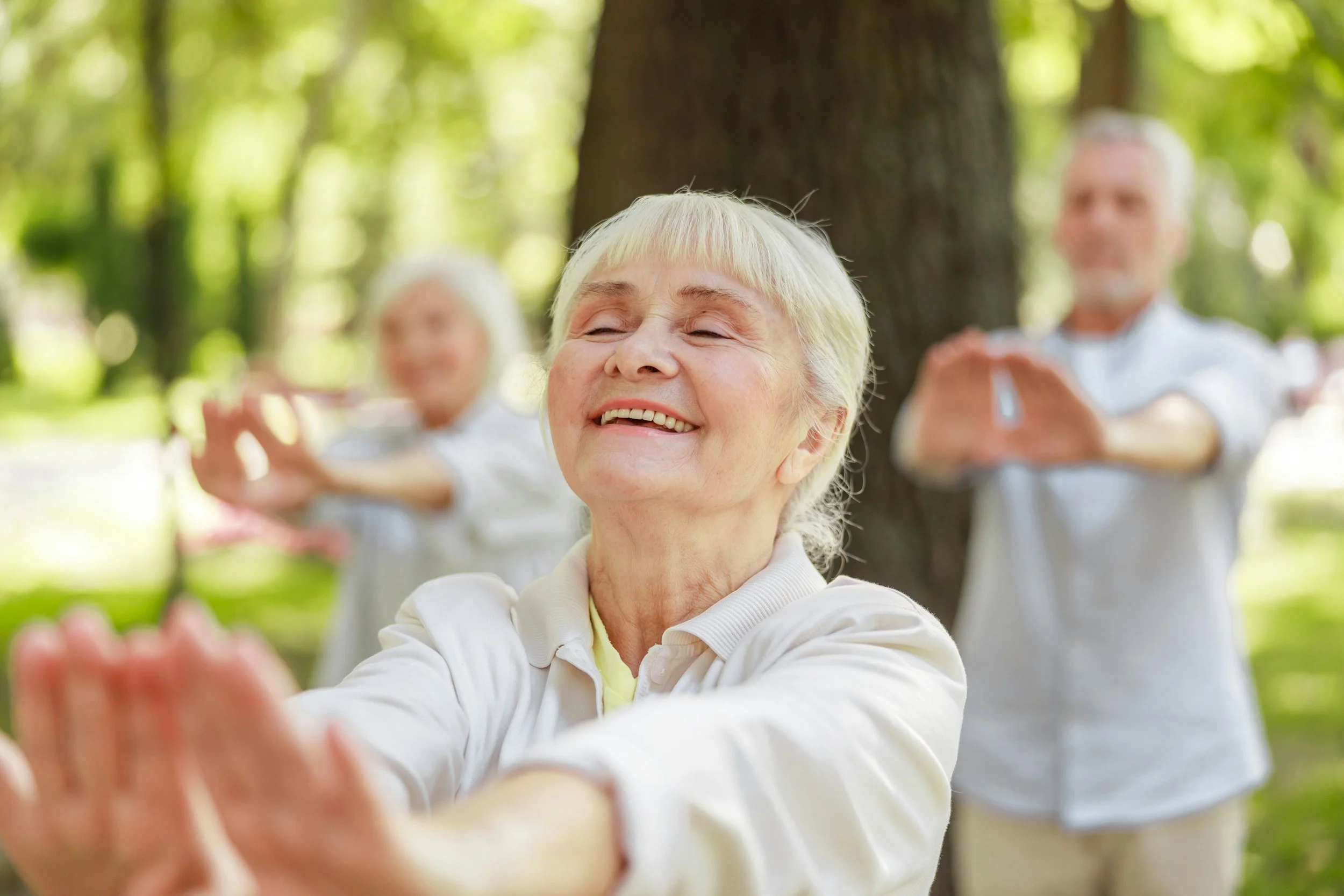 Idosas praticando yoga ao ar livre em um parque, sorrindo e relaxando sob árvores verdes.