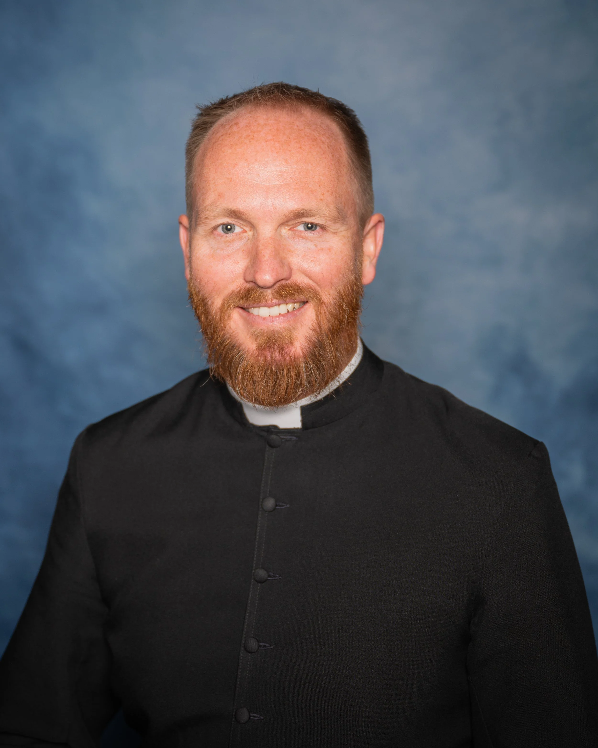 Priest clergy attire with a white collar, smiling.