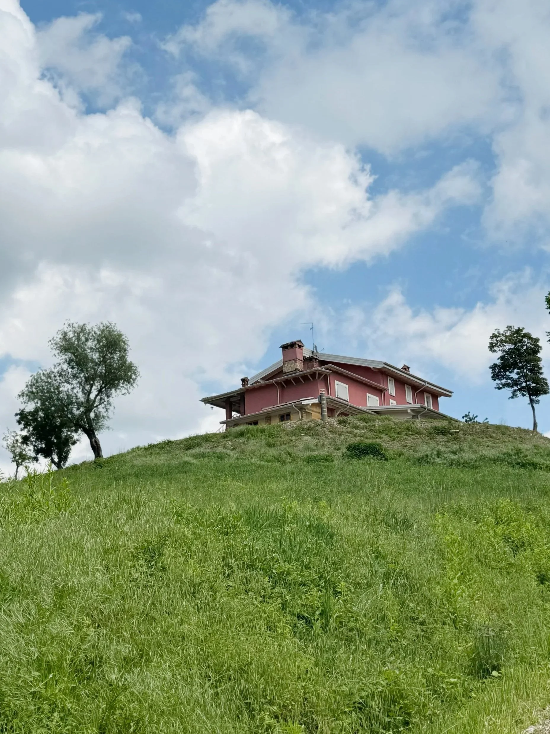 Casa immersa nel verde delle colline, con prato rigoglioso e cielo azzurro con nuvole bianche.