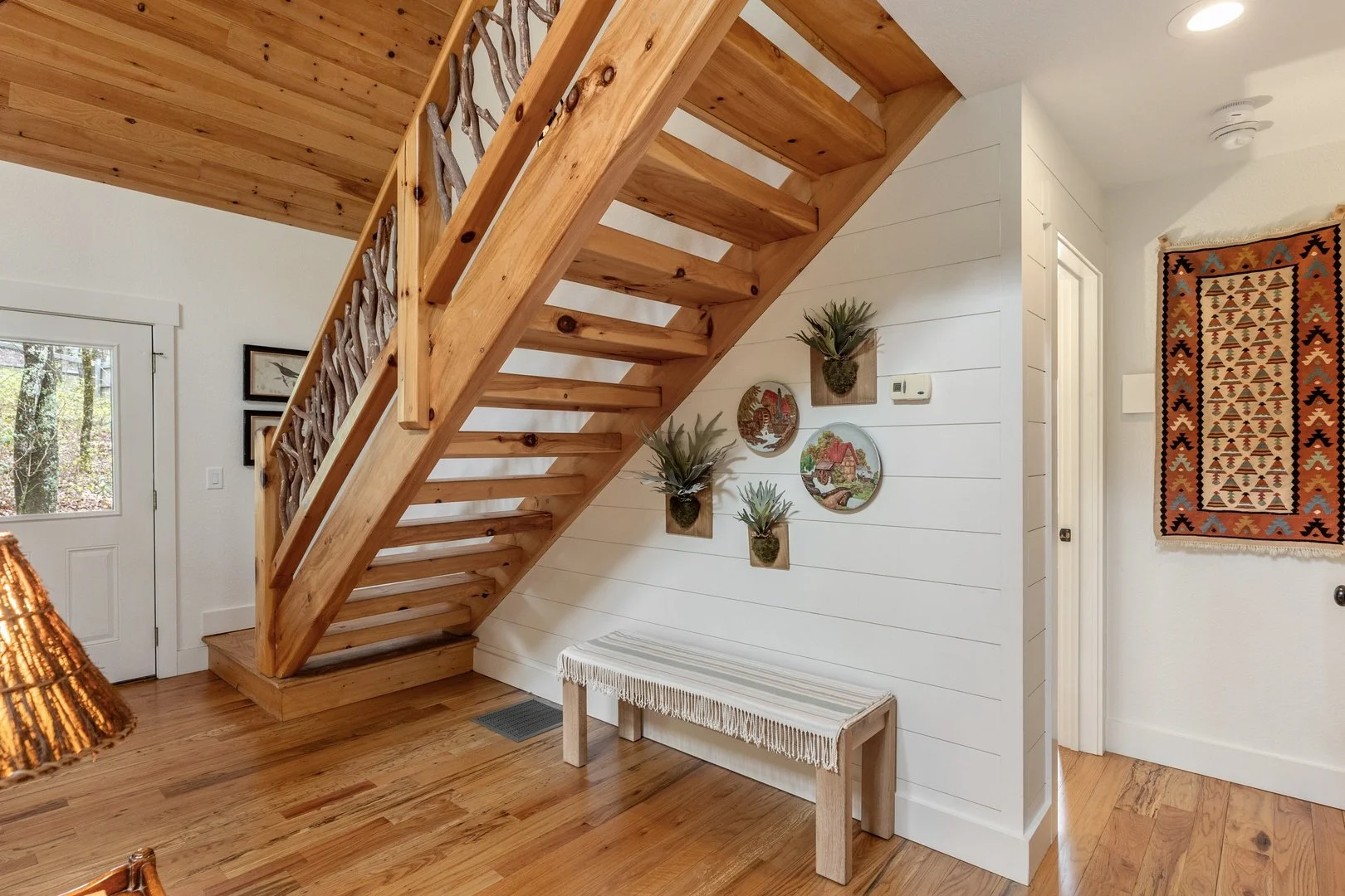 Creekwood Cottage’s entryway with a white bench and timber staircase.
