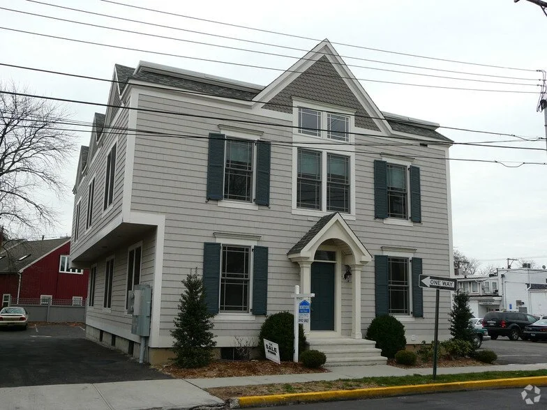 Three-story white house with dark shutters, gabled roof, and small front porch