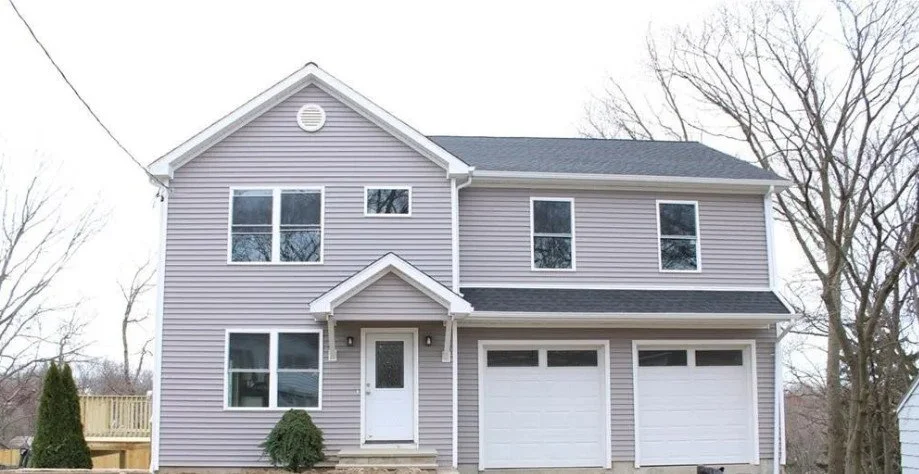 A two-story gray house with white trim, two garage doors, and a small porch with a door, surrounded by leafless trees.
