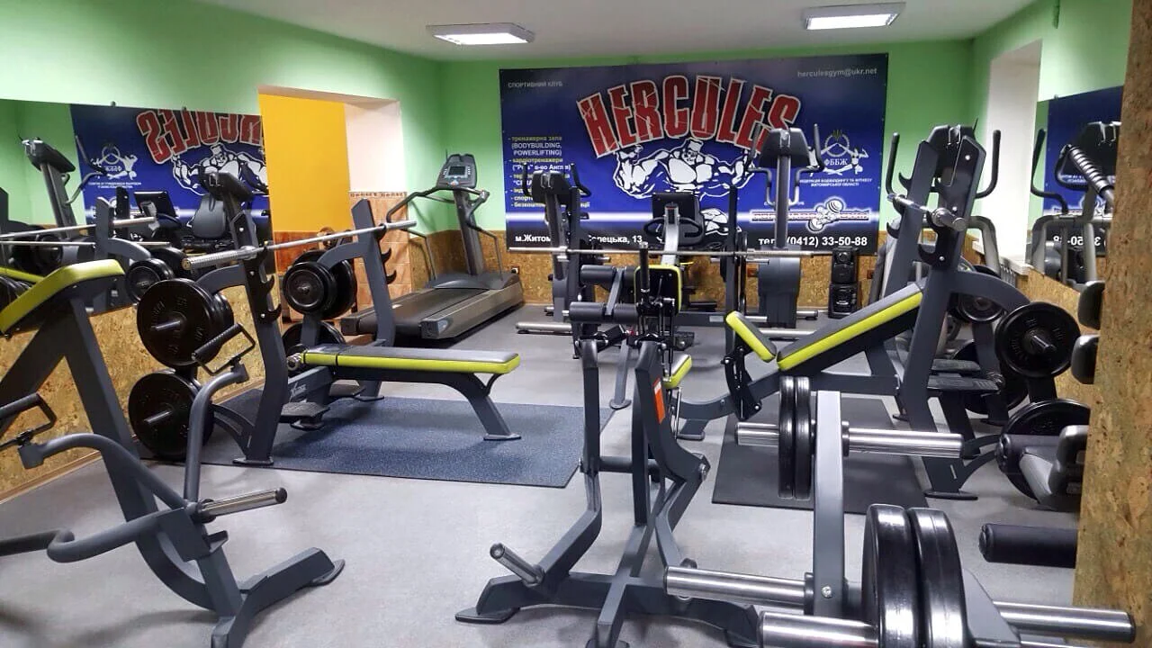 A small gym with various workout equipment, including treadmills, weight benches, and weightlifting machines, in a room with light green walls and mirrors.