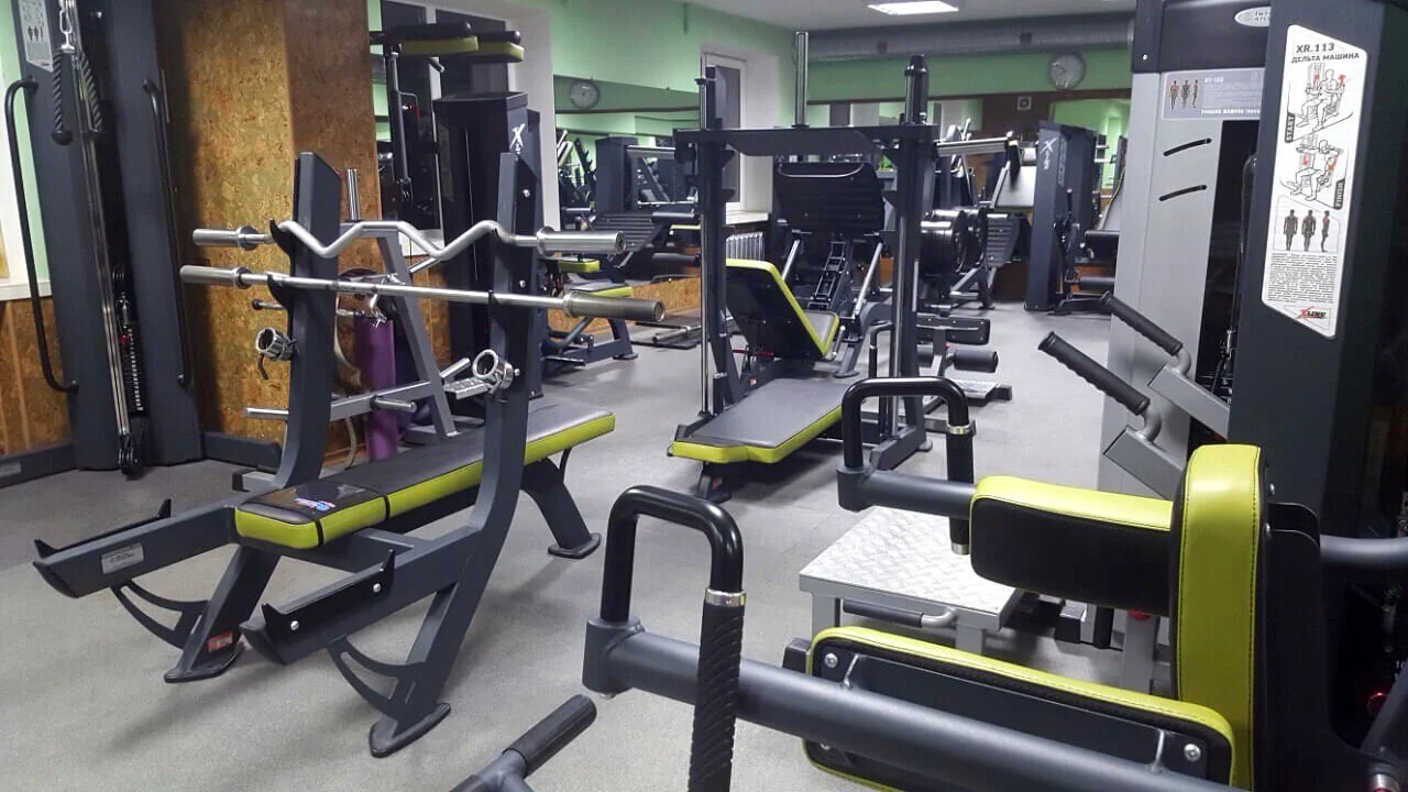 Gym with various workout equipment including benches, weight machines, and free weights in a well-lit fitness center.