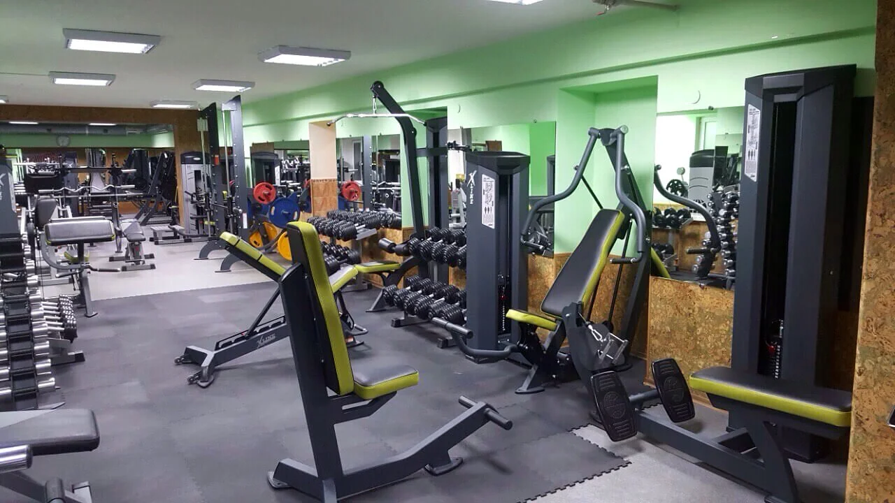 Interior of a gym with various workout equipment including weight machines, free weights, benches, and cardio machines.
