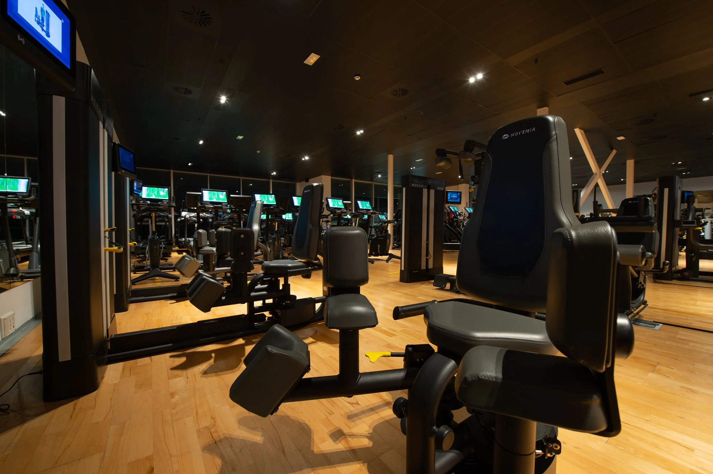 Empty fitness gym with various workout machines, including exercise bikes, and a wooden floor.
