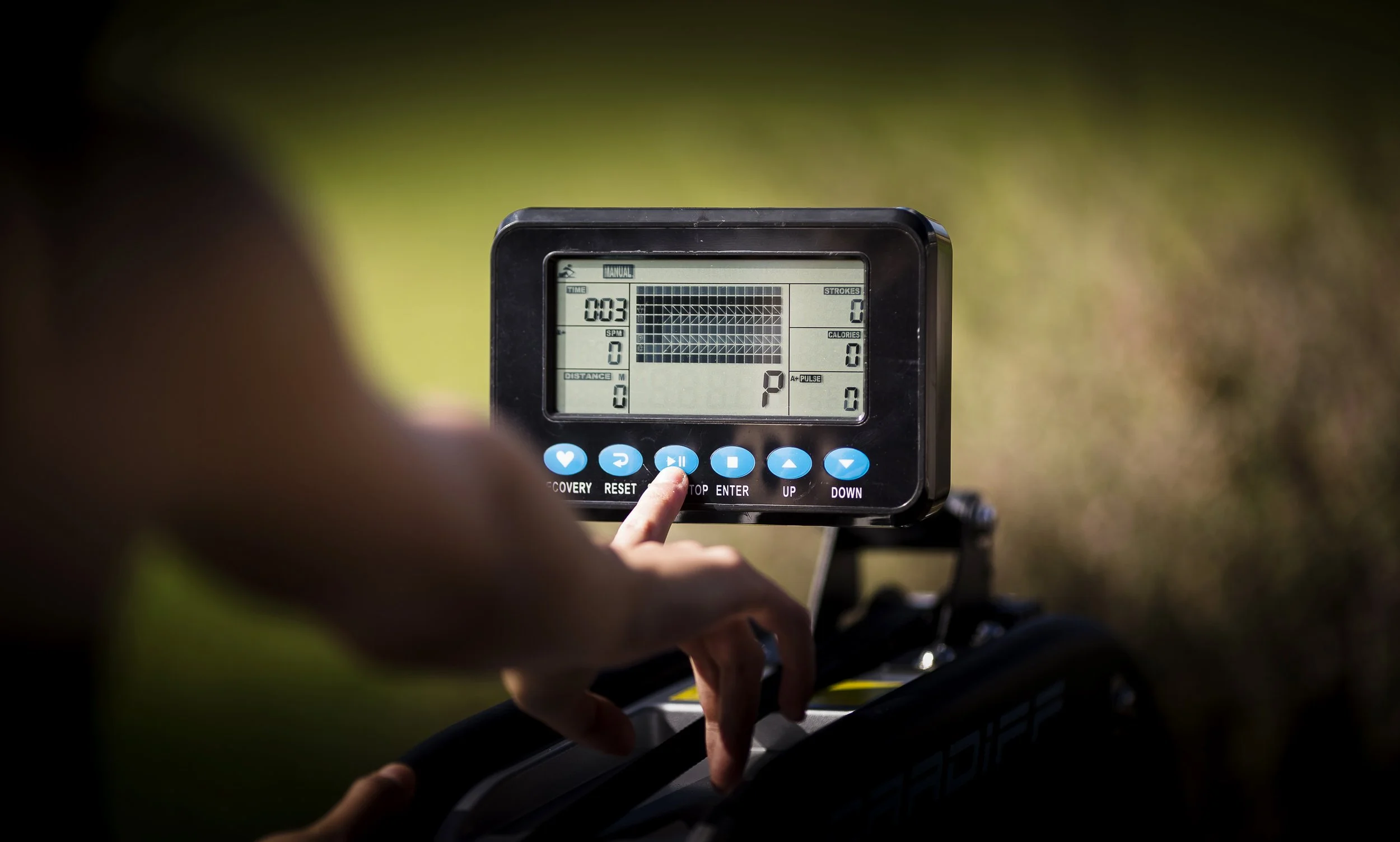Close-up of a person operating a digital treadmill console outdoors, with controls and a display screen showing workout statistics.