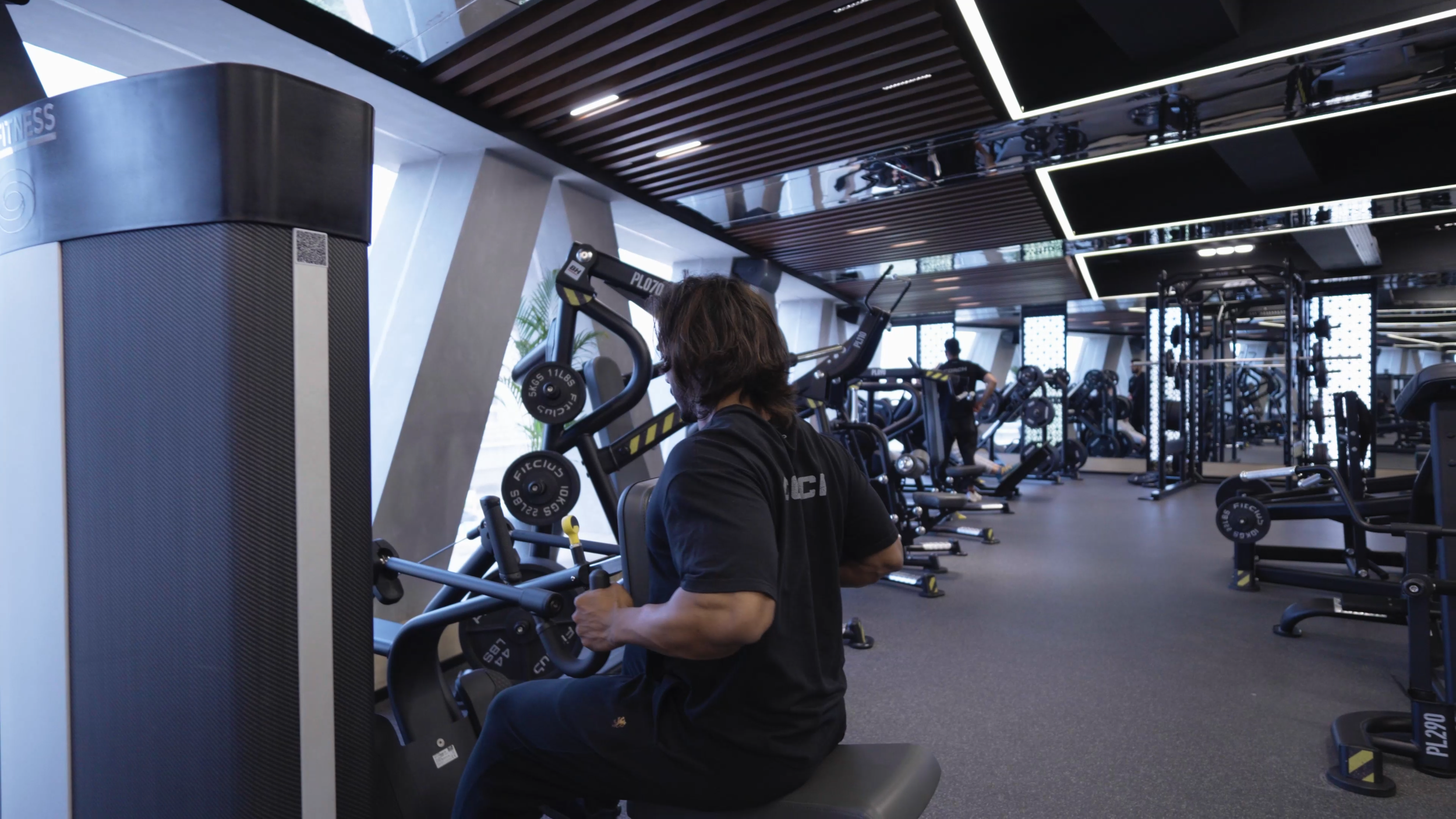 Person using a chest press machine at a gym with various workout equipment in the background.