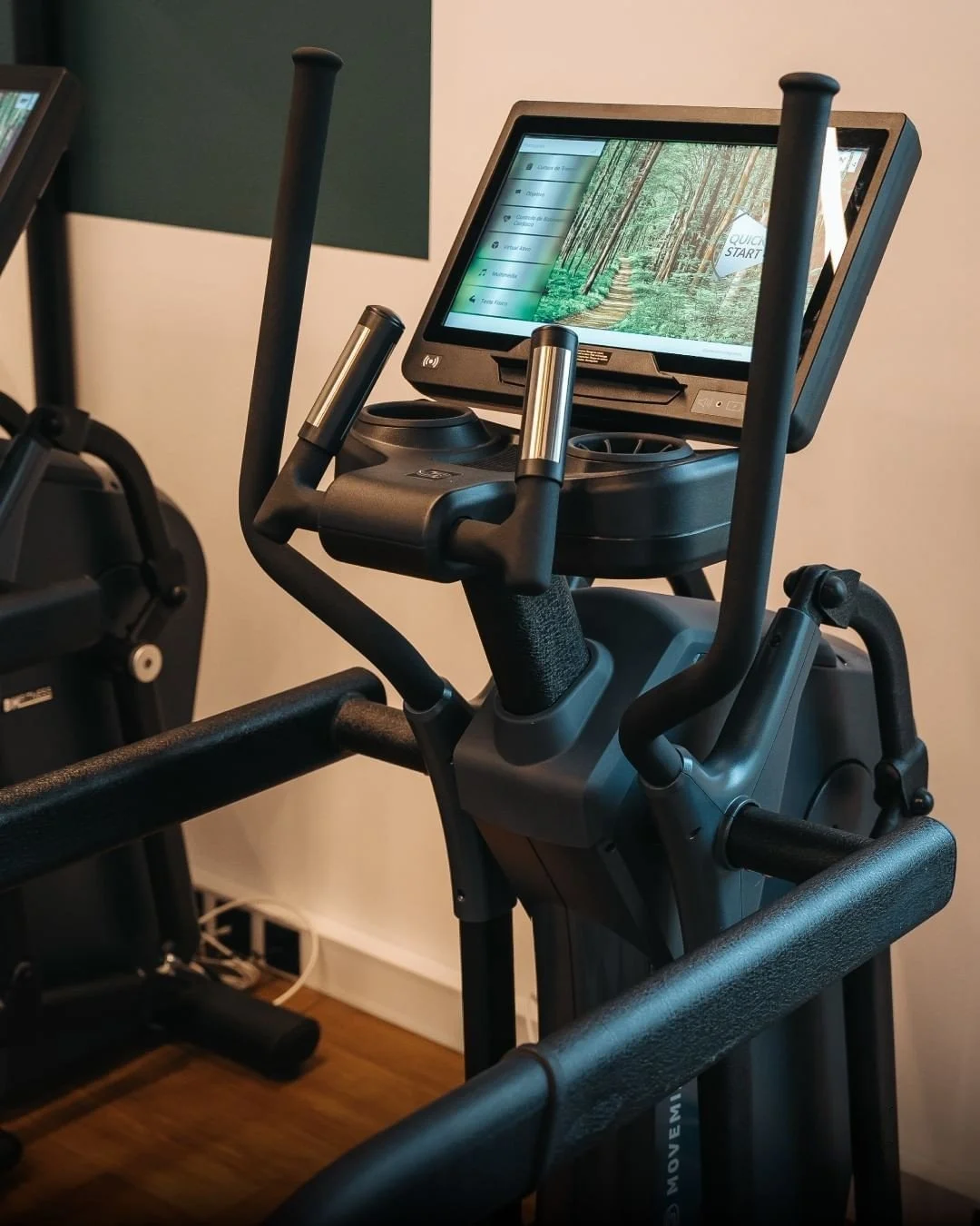 A fitness elliptical machine with a digital display screen showing a nature scene and workout options.
