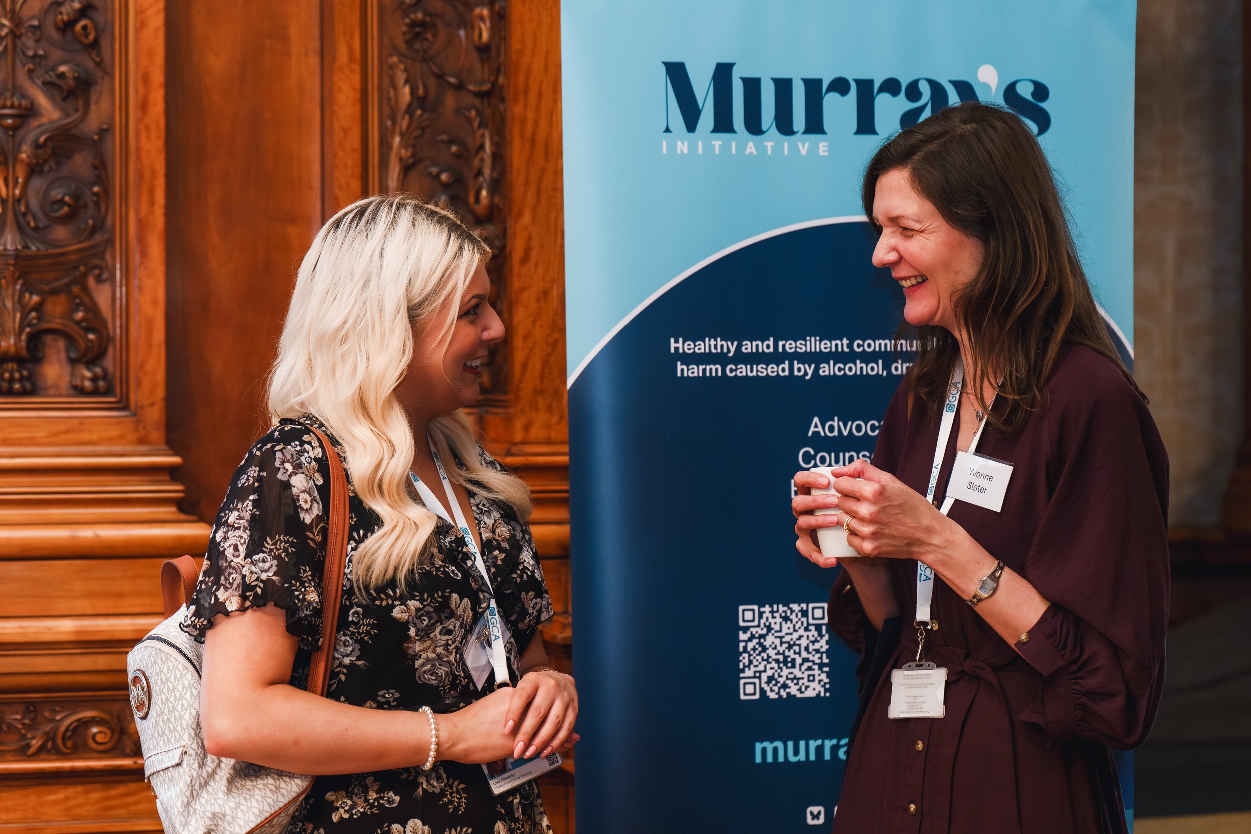 Image of 2 people having a conversation in front of Murray's Initiative banner.